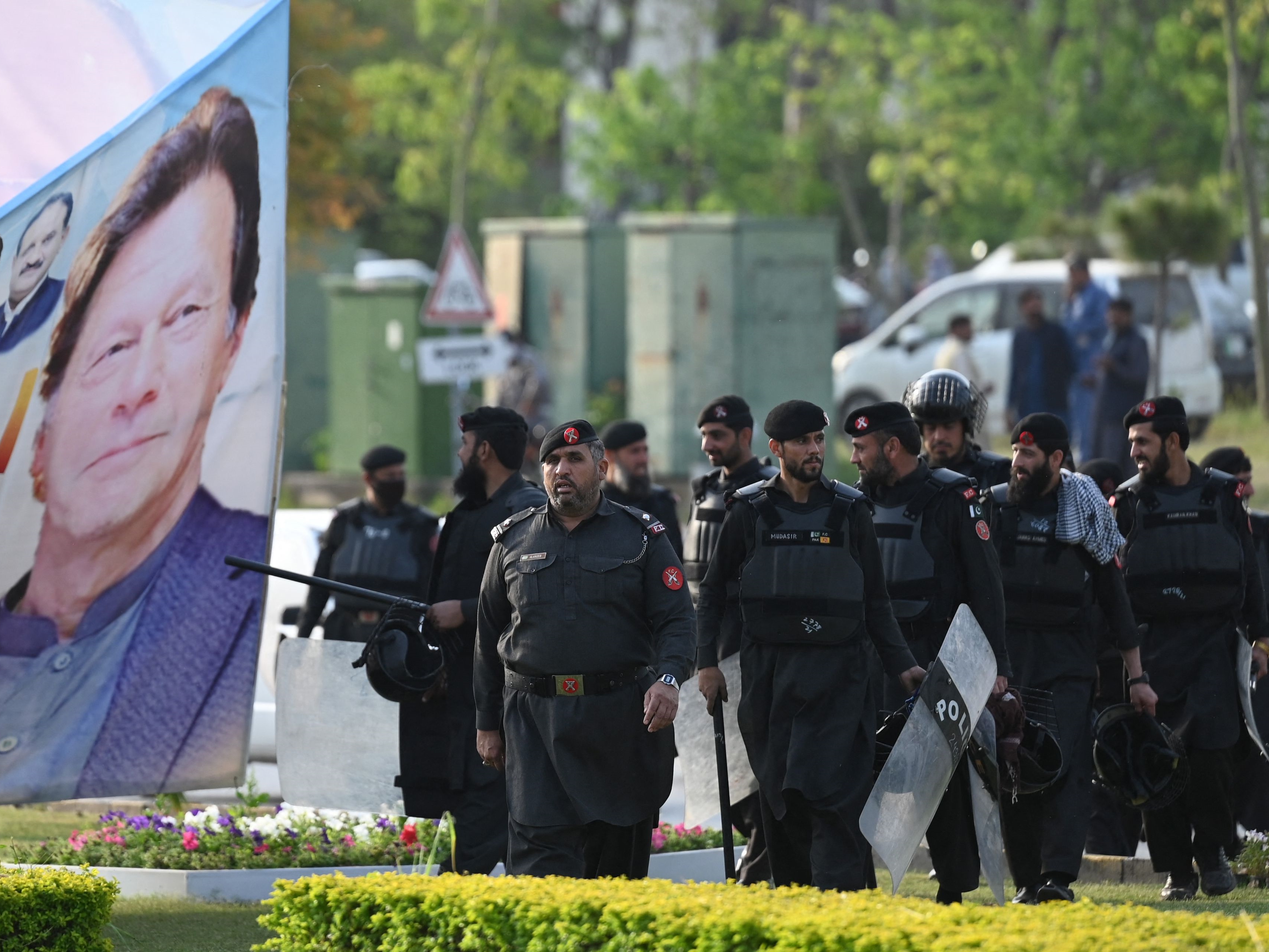 Personel keamanan berjalan melewati spanduk yang menampilkan gambar Perdana Menteri Pakistan Imran Khan di dekat gedung Parlemen.