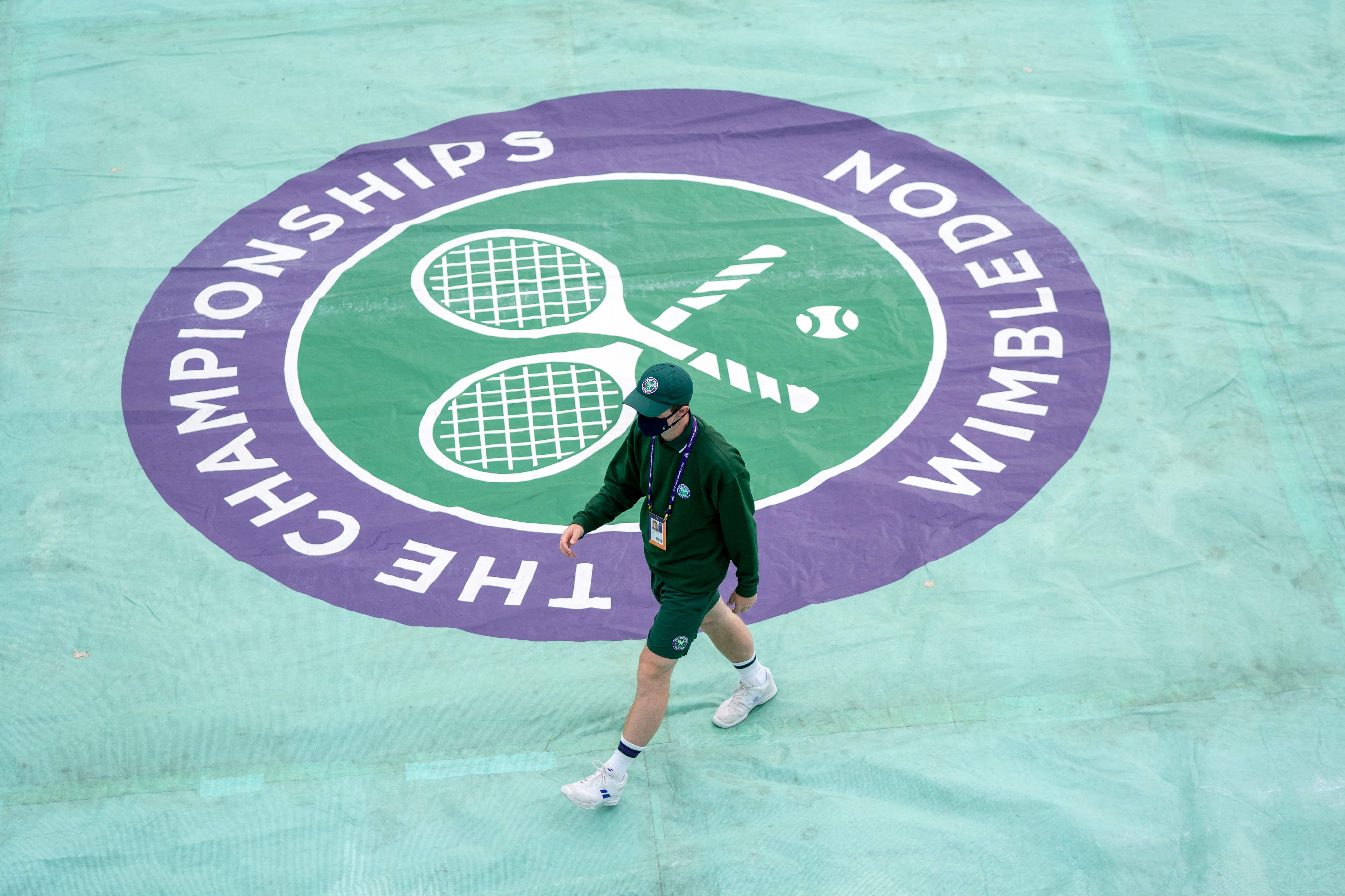 Seorang petugas melintas di depan logo Wimbledon yang ada di The All England Tennis Club, Wimbledon, Inggris.