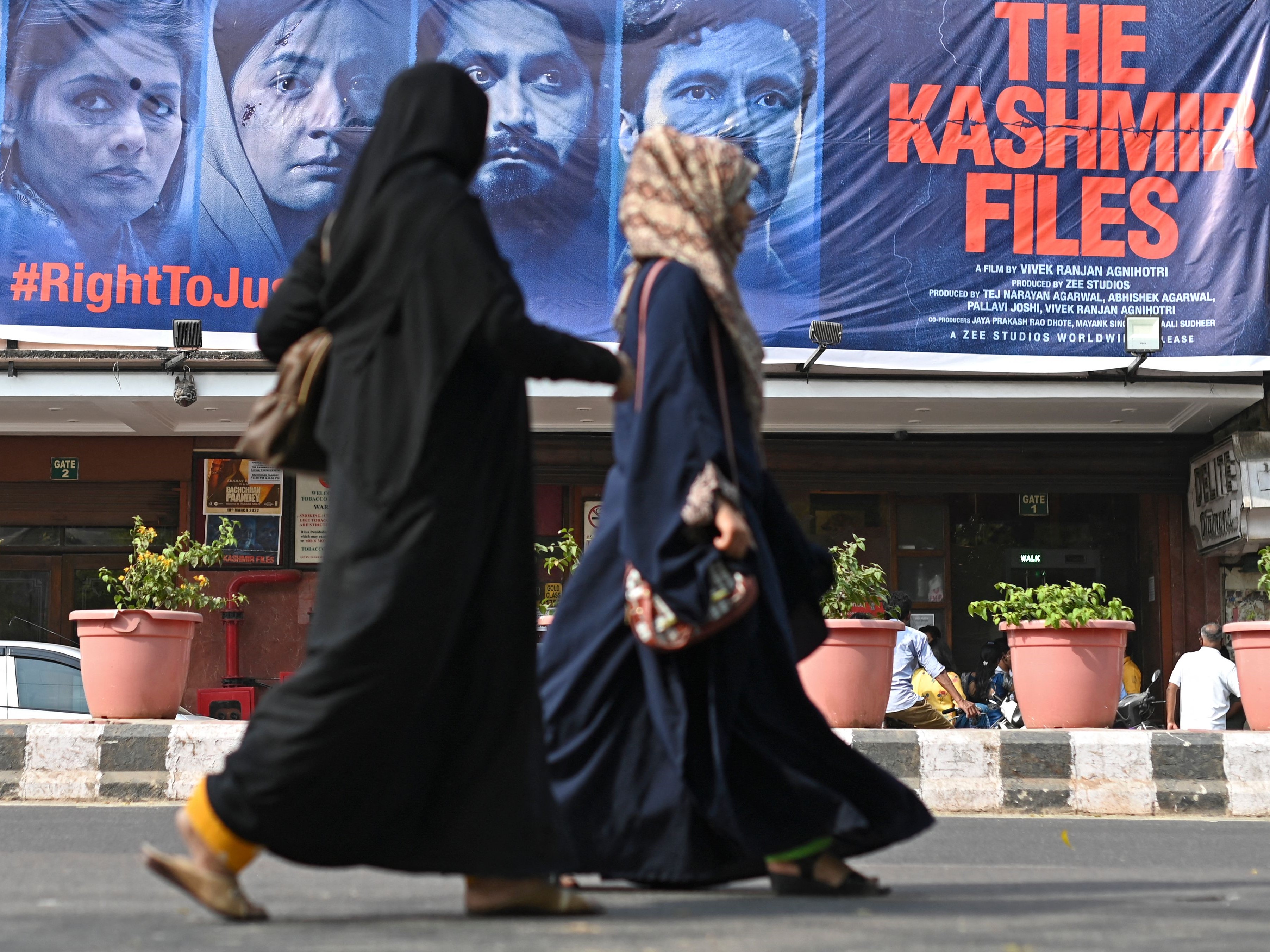 Para wanita berjalan melewati spanduk film Bollywood The Kashmir Files di luar gedung bioskop, 21 Maret 2022, Delhi, India.