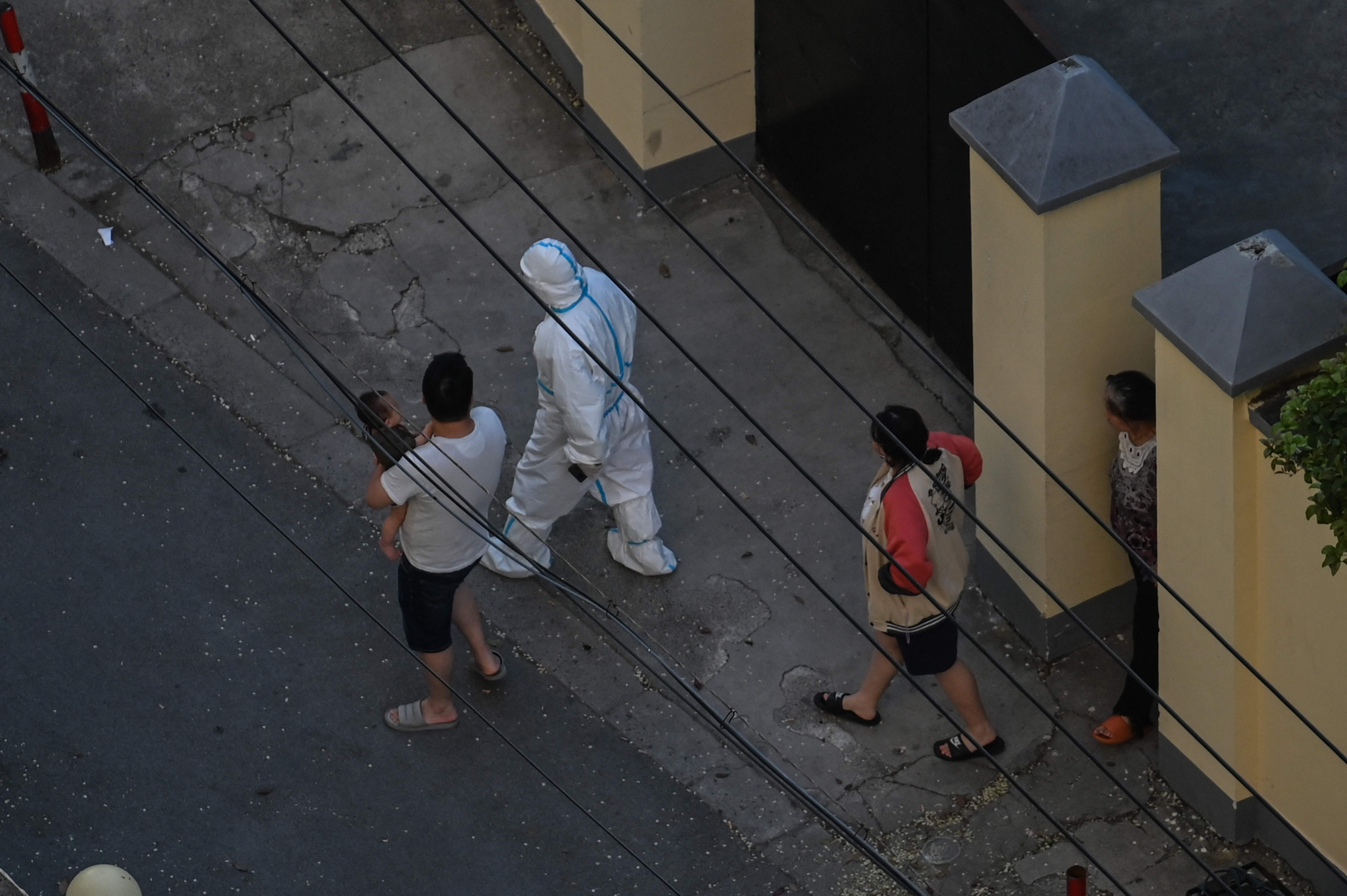 Tenagah kesehatan mengenakan APB berjalan bersama warga yang tengah menjalani lockdown di Distrik Jing'an, Shanghai, Tiongkok.