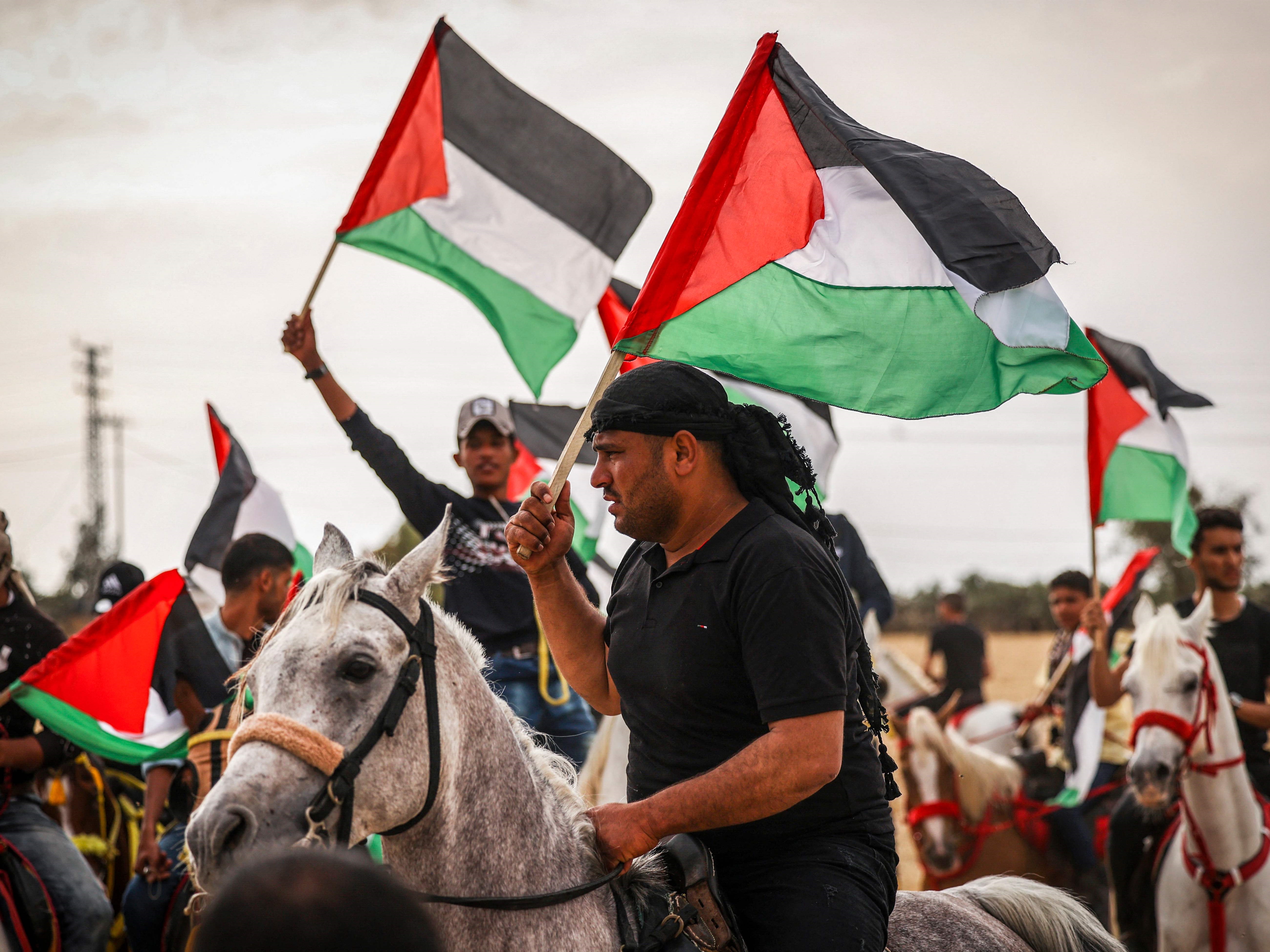 Warga Palestina mengibarkan bendera nasional mereka mengambil bagian di atas kuda dalam unjuk rasa pada peringatan 74 tahun Nakba.
