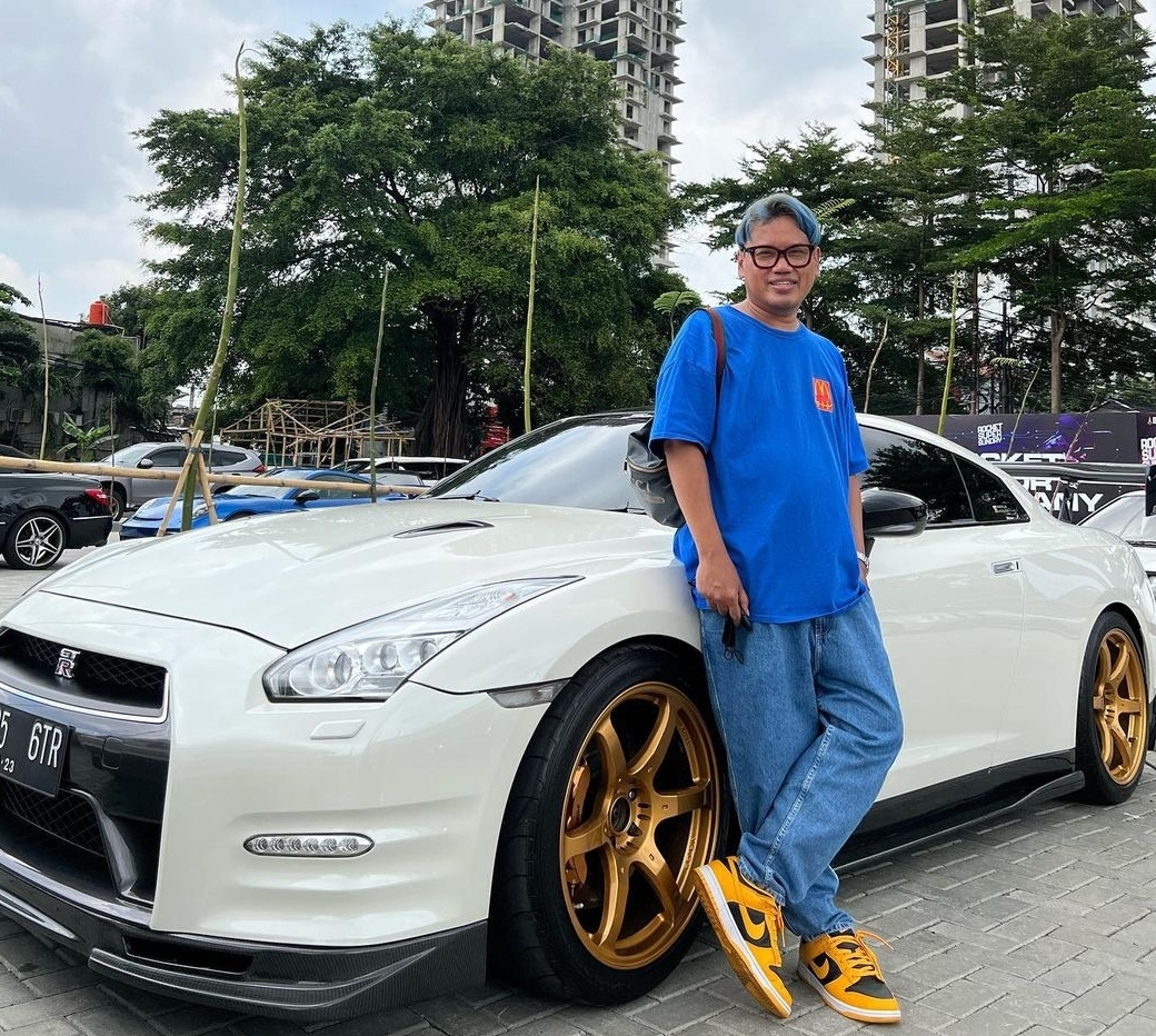 Artis Uya Kuya tengah berpose di dekat sebuah kendaraan mewah.