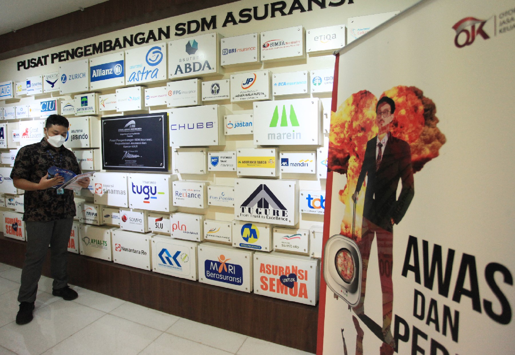 Karyawan berdiri dekat logo perusahaan asuransi yang ada di Indonesia.