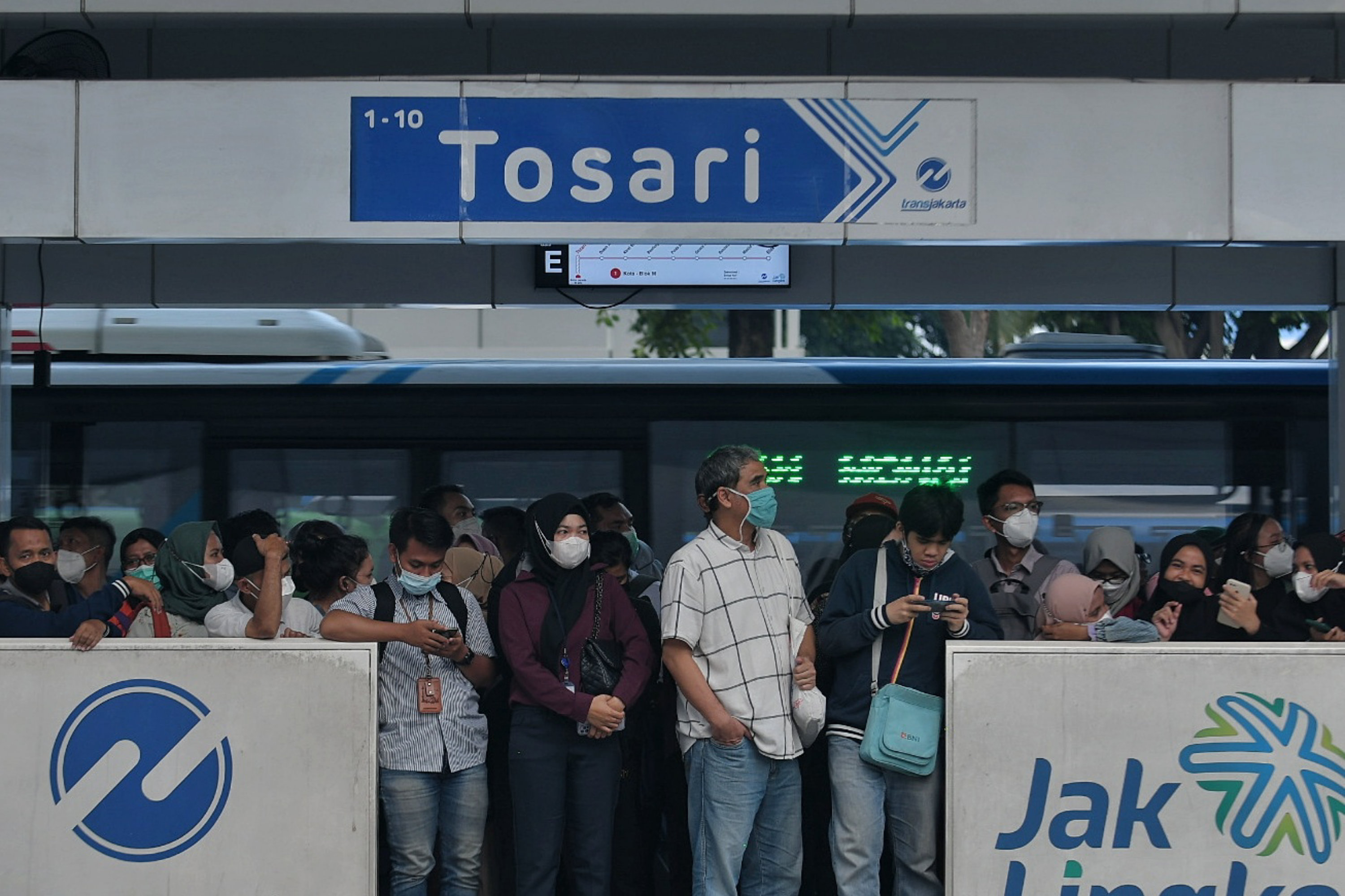 Penumpang TransJakarta menunggu di halte dengan menerapkan protokol kesehatan menggunakan masker