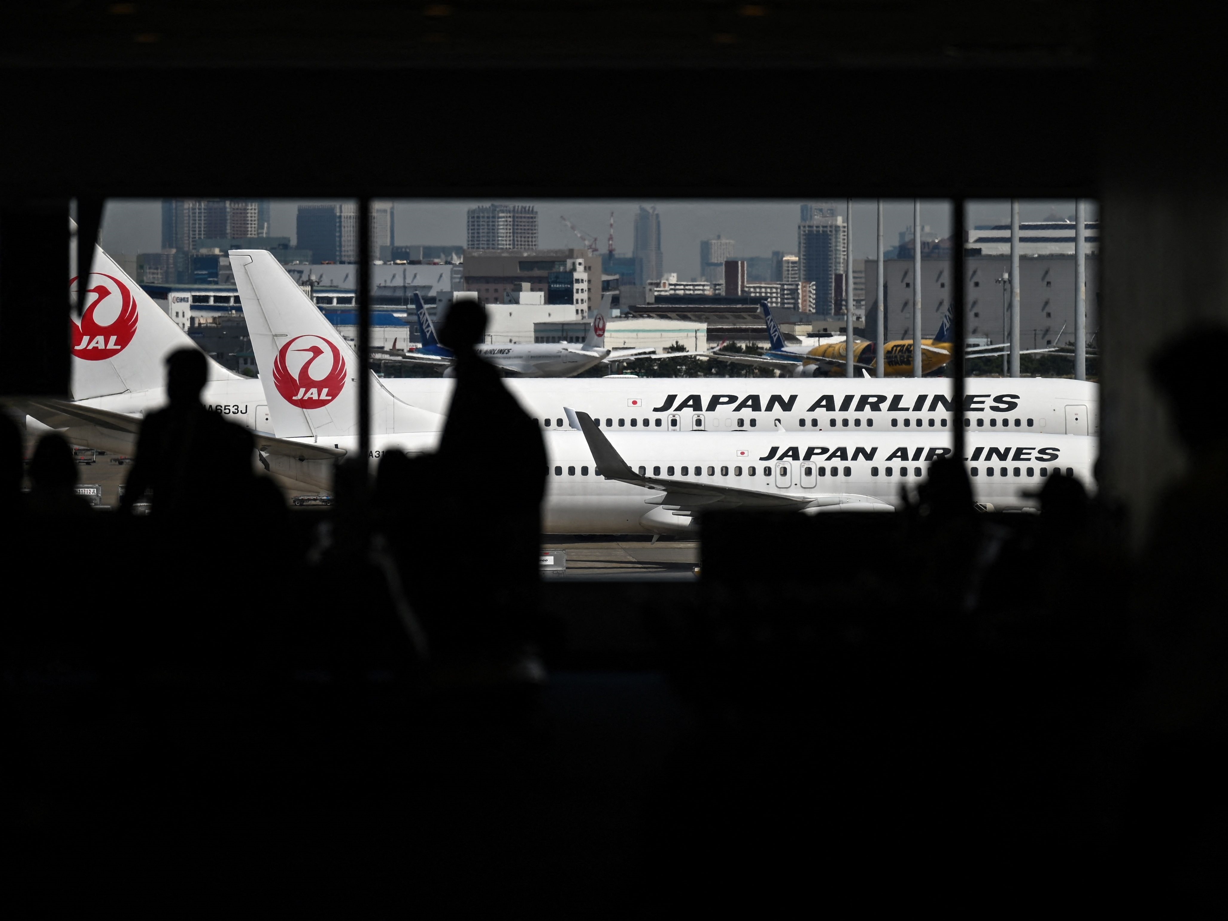 Siluet orang-orang saat pesawat Japan Airlines (JAL) terlihat di landasan Bandara Internasional Tokyo di Haneda. 