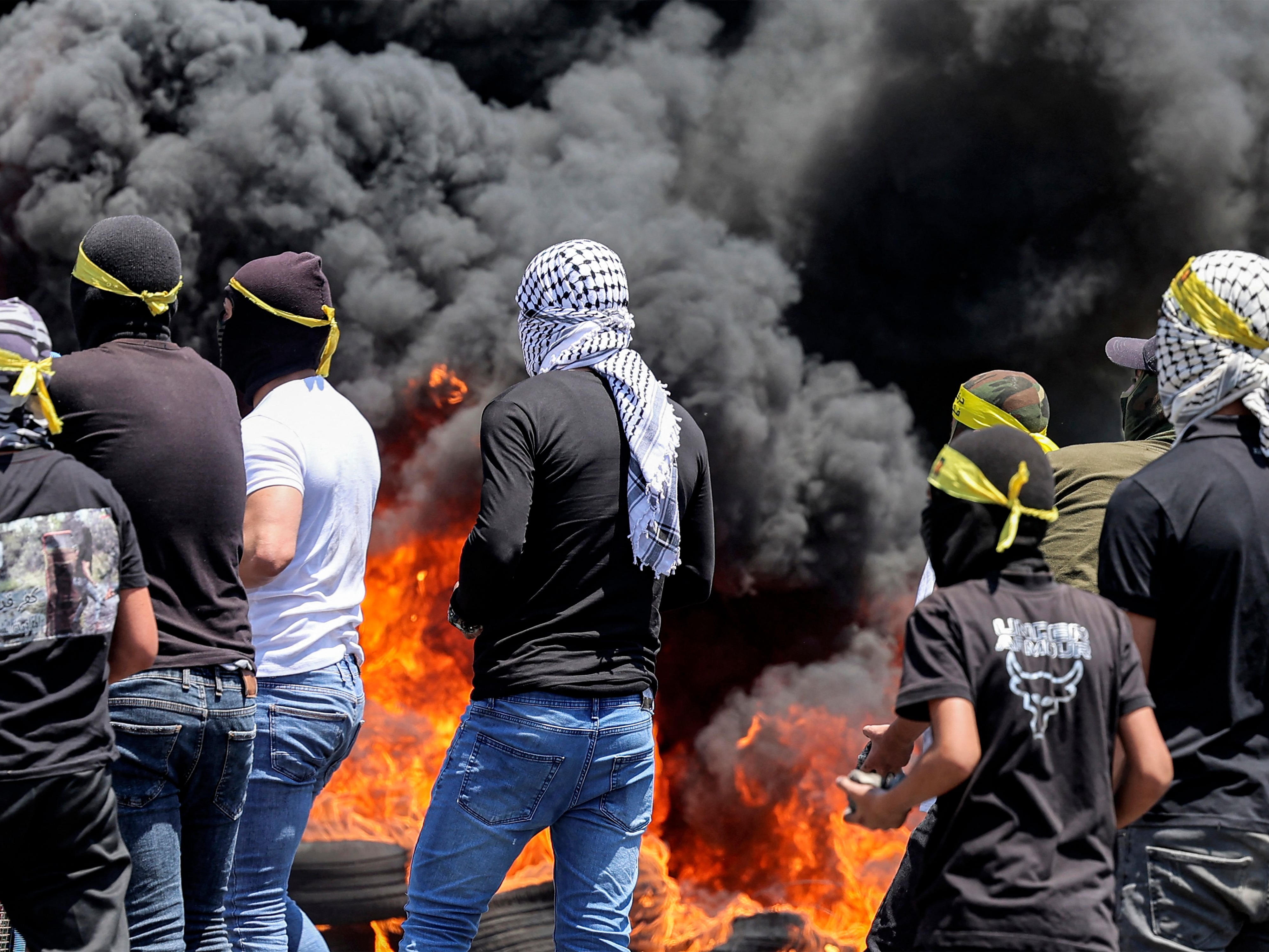 Para pengunjuk rasa berdiri memegang batu di depan asap dari ban yang terbakar selama bentrokan dengan pasukan Israel.