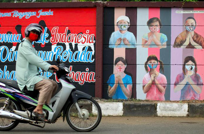 Warga melintas dekat mural bergambar simbol orang berdoa menggunakan masker yang mewakili umat beragama di Indonesia di Jalan Juanda, Depok 