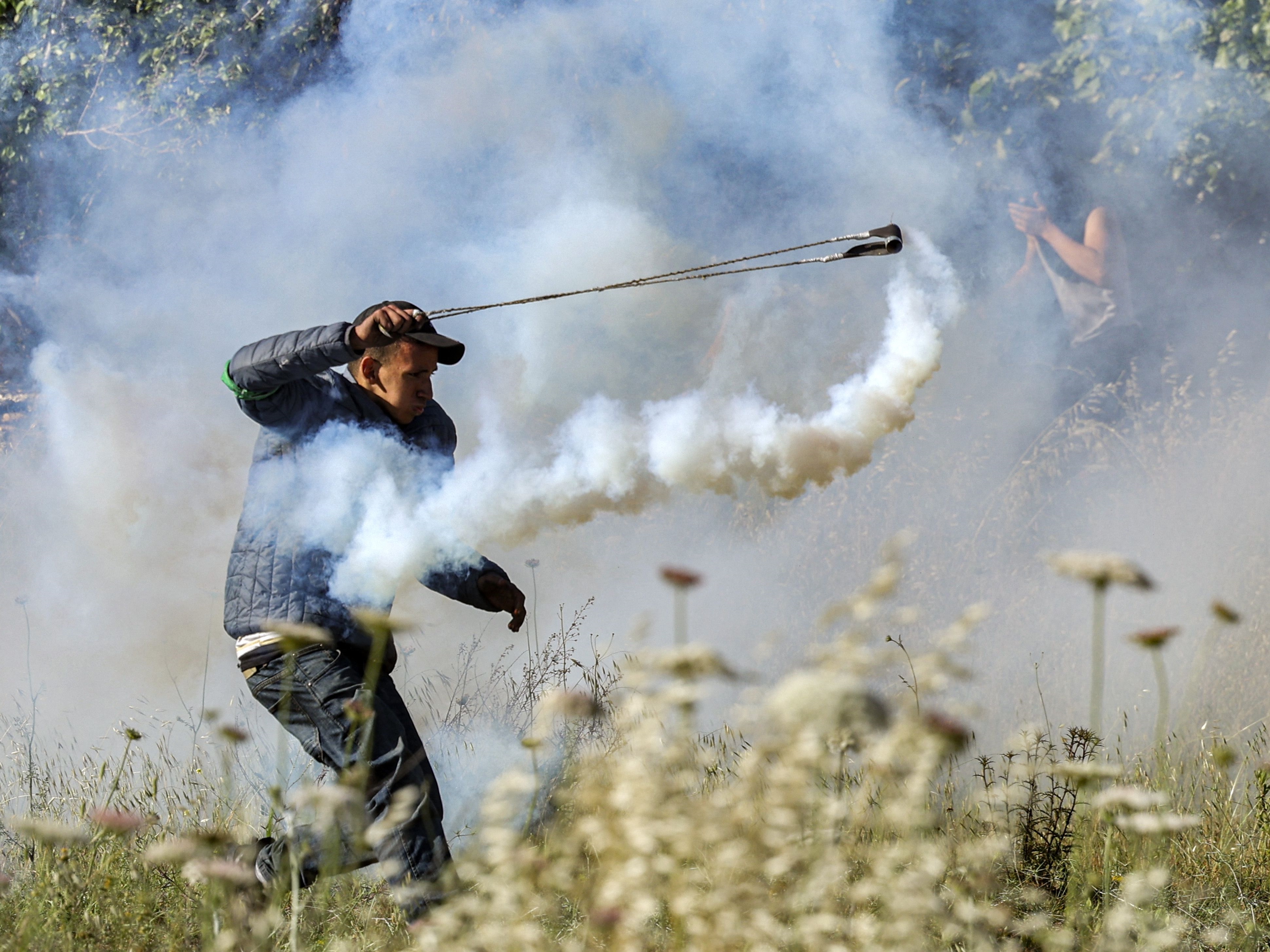 Seorang pengunjuk rasa Palestina menggunakan ketapel untuk melemparkan kembali tabung gas air mata ke pasukan Israel selama bentrok.