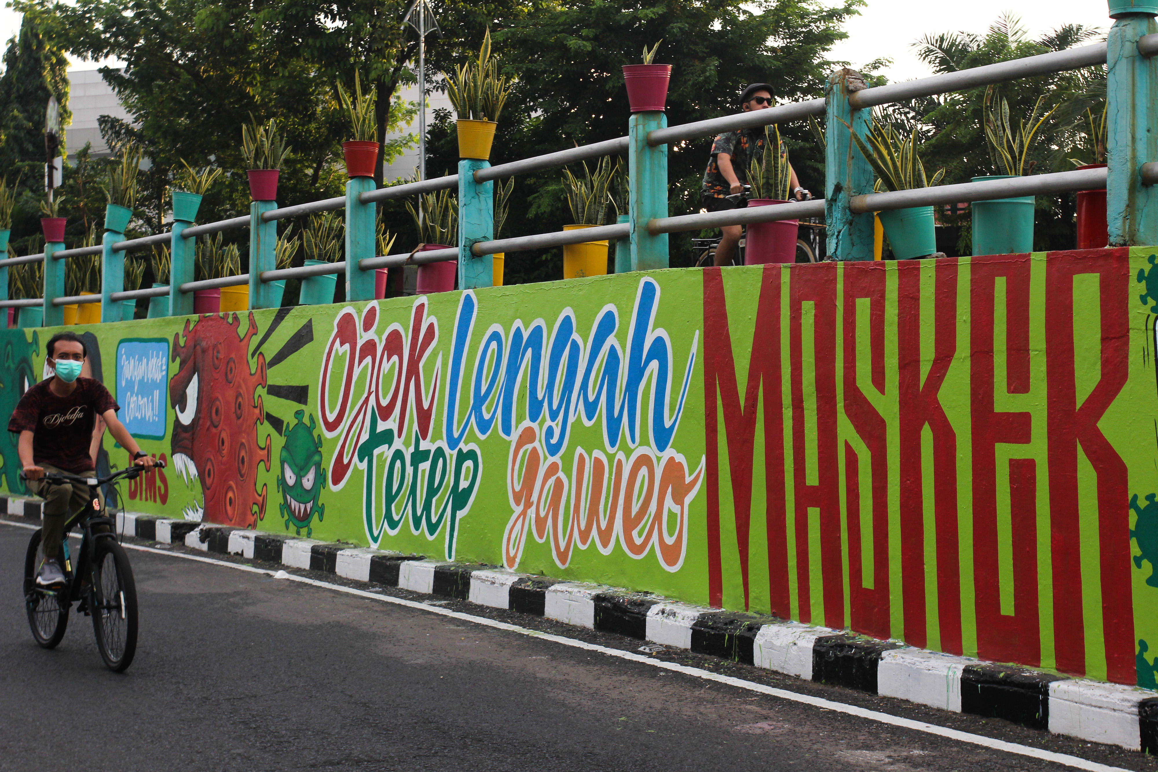 Pesepeda melintas di dekat dinding bermural di Surabaya, Jawa Timur.