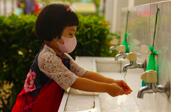 Seorang anak yang mengenakan masker sedang mencuci tangan