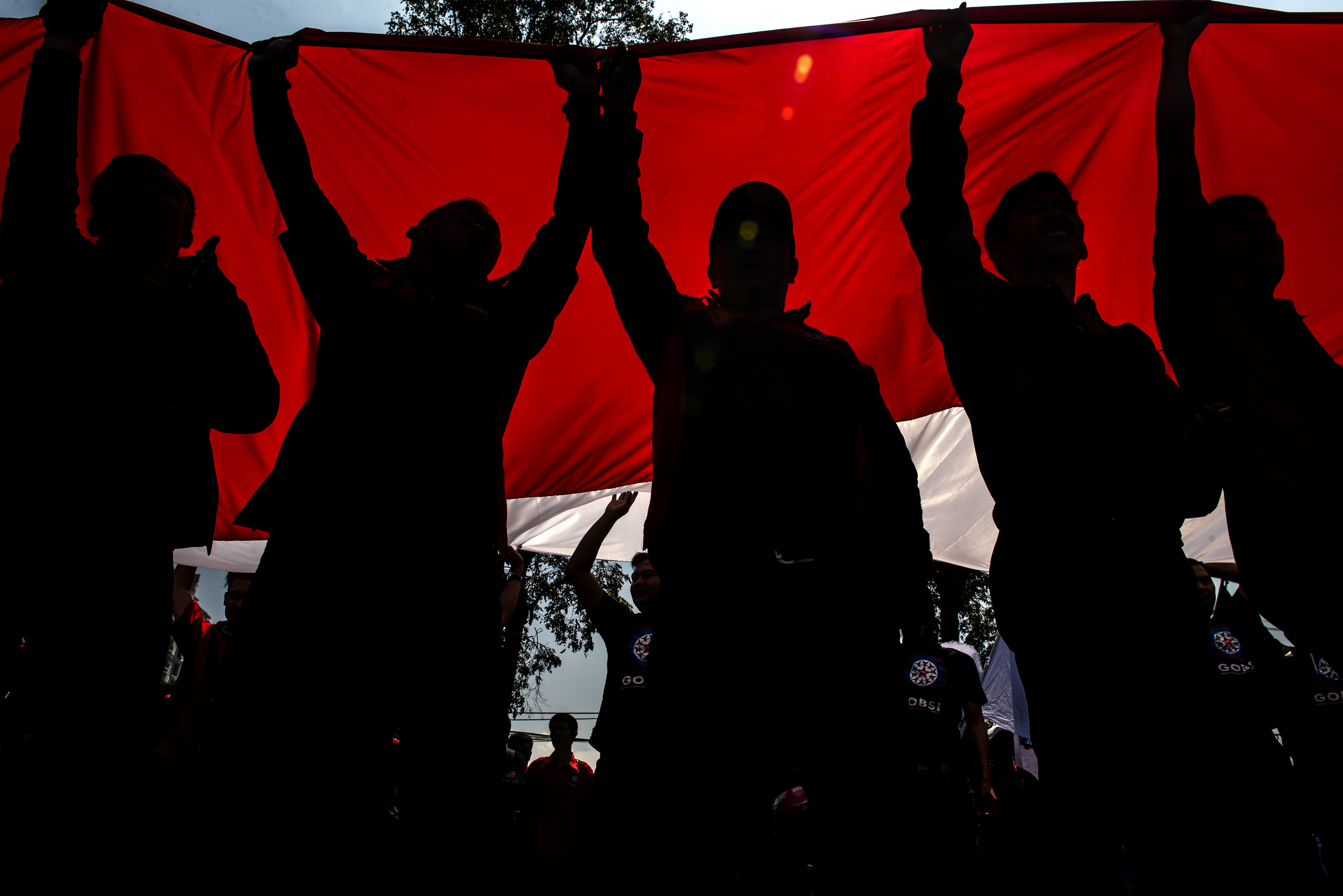 Siluet buruh membawa bendera merah putih saat aksi Hari Buruh Internasional di depan Gedung Sate, Bandung, Jawa Barat.