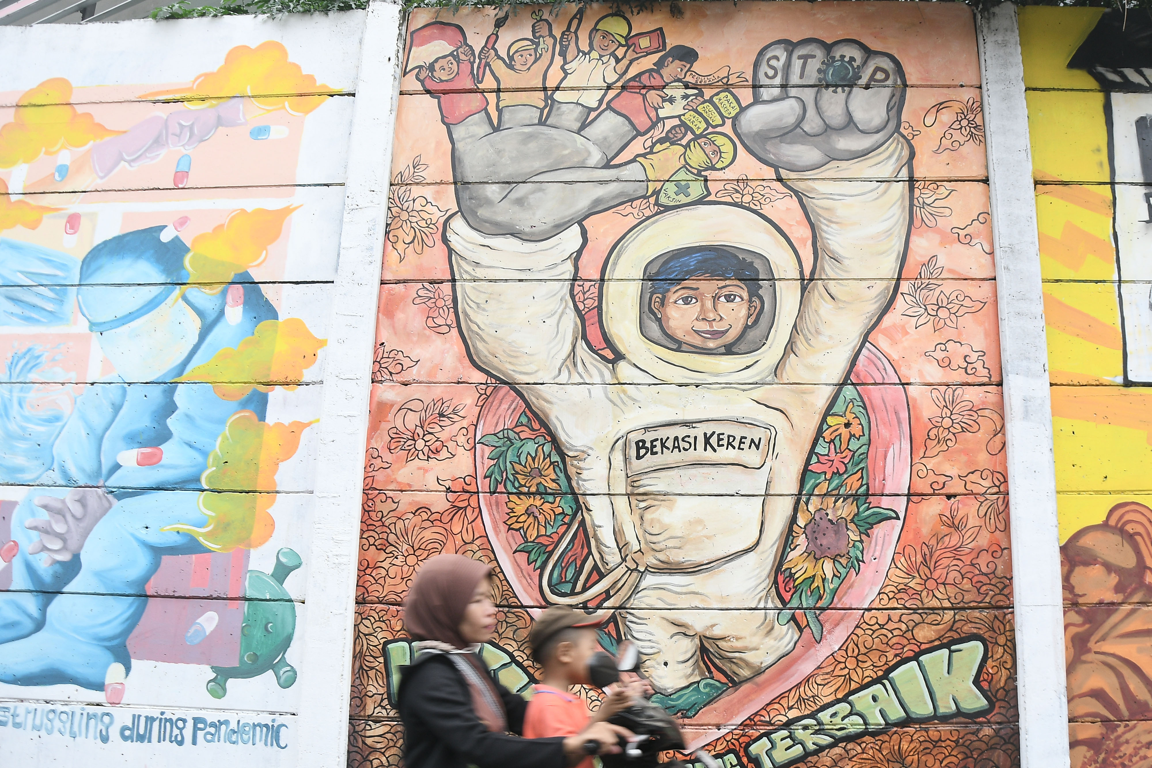 Dua orang warga melintasi mural bertemakan covid-19 di Bekasi, Jawa Barat.