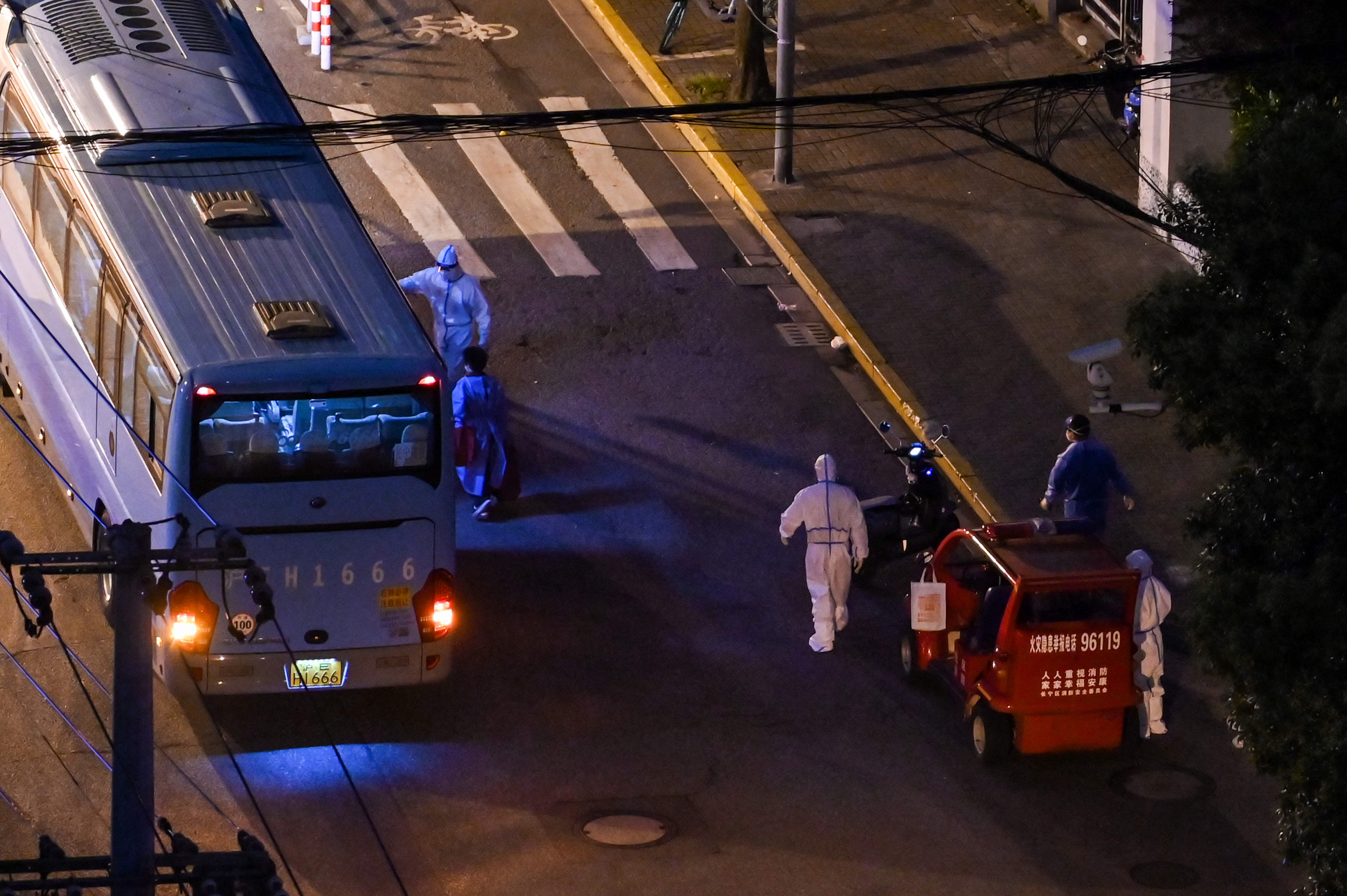 Petugas medis dengan pelindung diri memeriksa penumpang yang turun dari bus di Distrik Jing'an, Kota Shanghai, Tiongkok, Sabtu (14/5).  