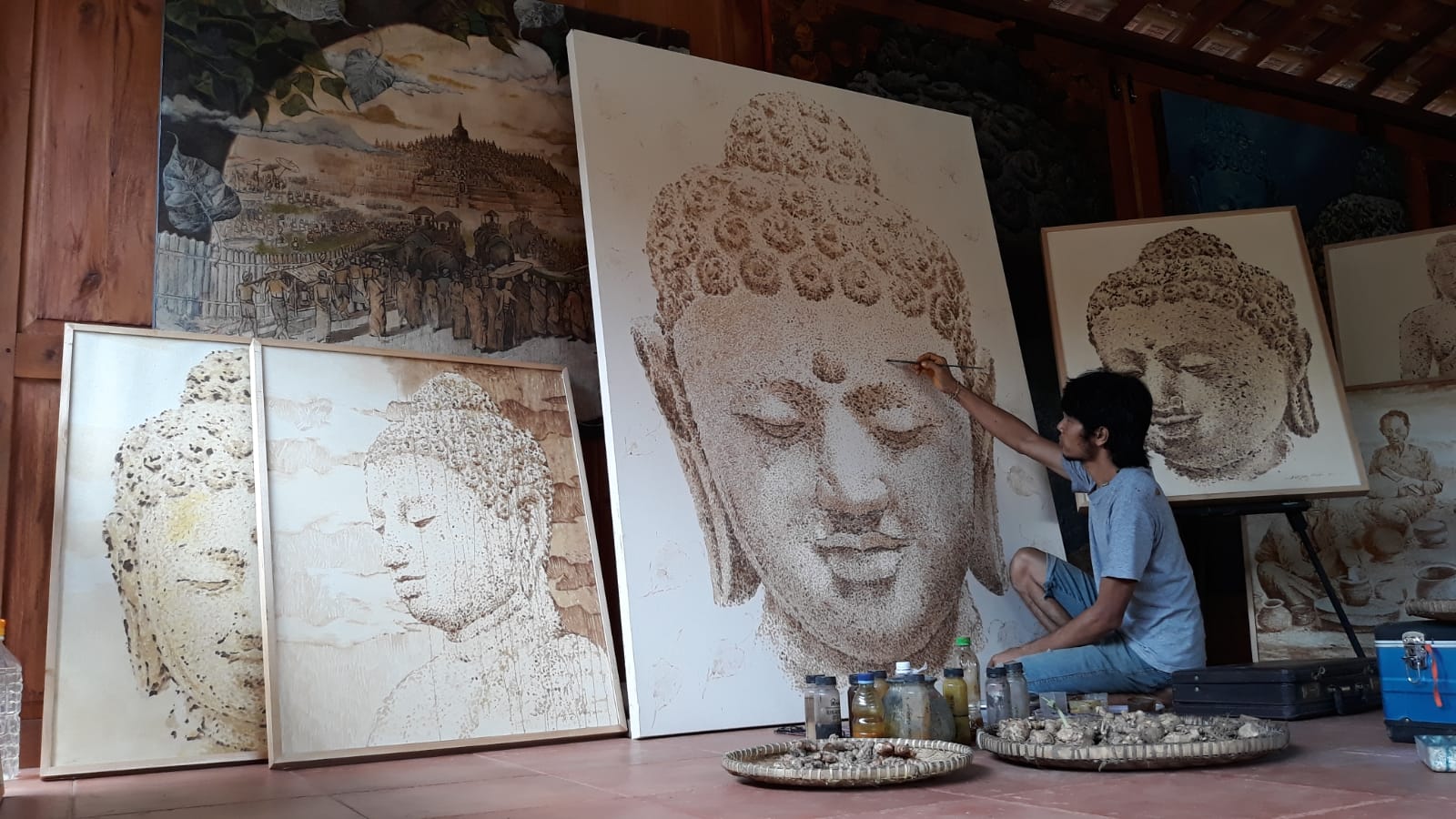 Pelukis Eastingmedi sedang melukis kepala Budha dengan cat lukisan terbuat dari rempah-rempah (empon-empon).