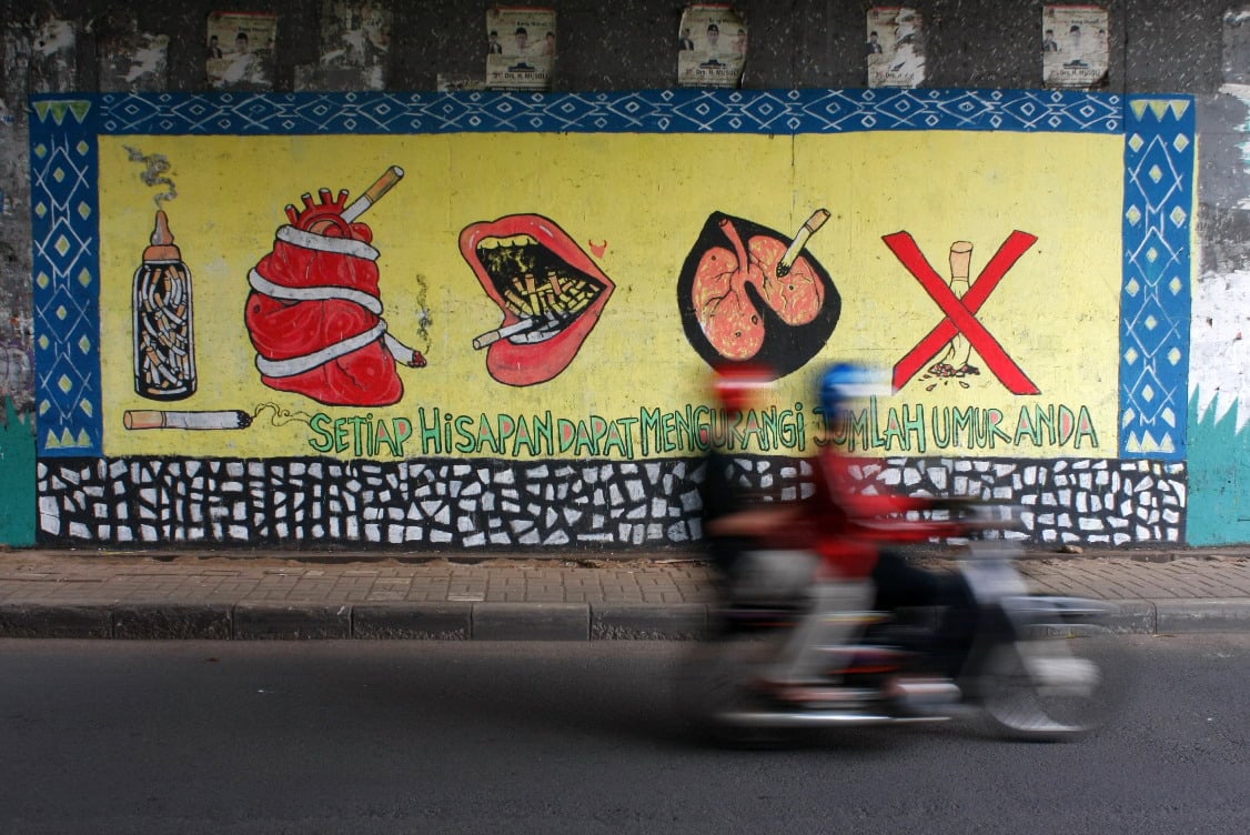 Pengendara bermotor tengah melintasi gambar mural peringatan bahaya merokok di terowongan Jalan Raya Margonda, Depok, Jawa Barat