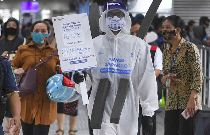 Anggota komunitas pecinta Transjakarta mengenakan baju hazmat melakukan sosialisasi protokol kesehatan di Halte Transjakarta Harmoni.