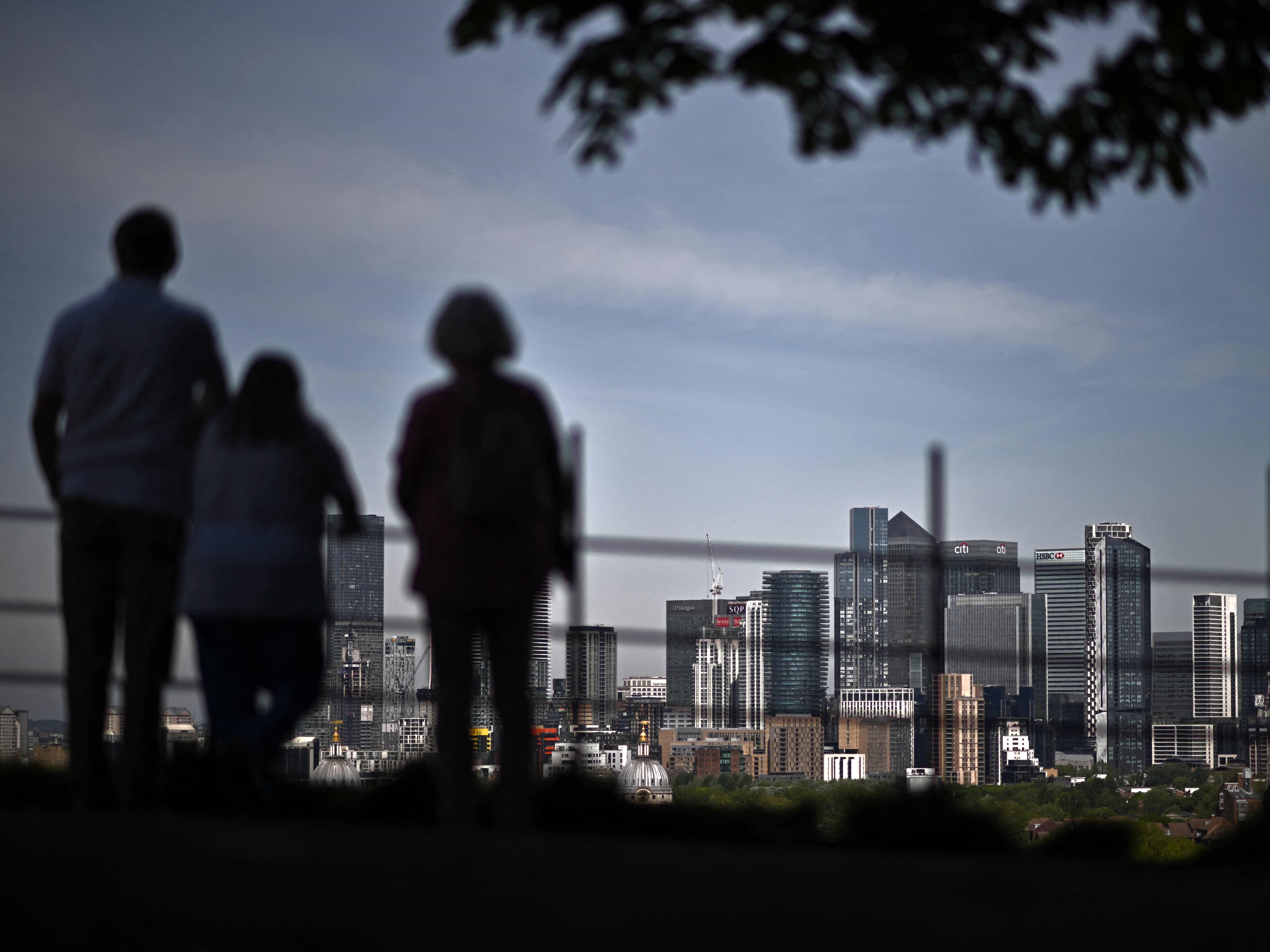 Orang-orang melihat ke distrik pusat bisnis sekunder London Canary Wharf di bawah sinar matahari musim semi dari Greenwich Park.