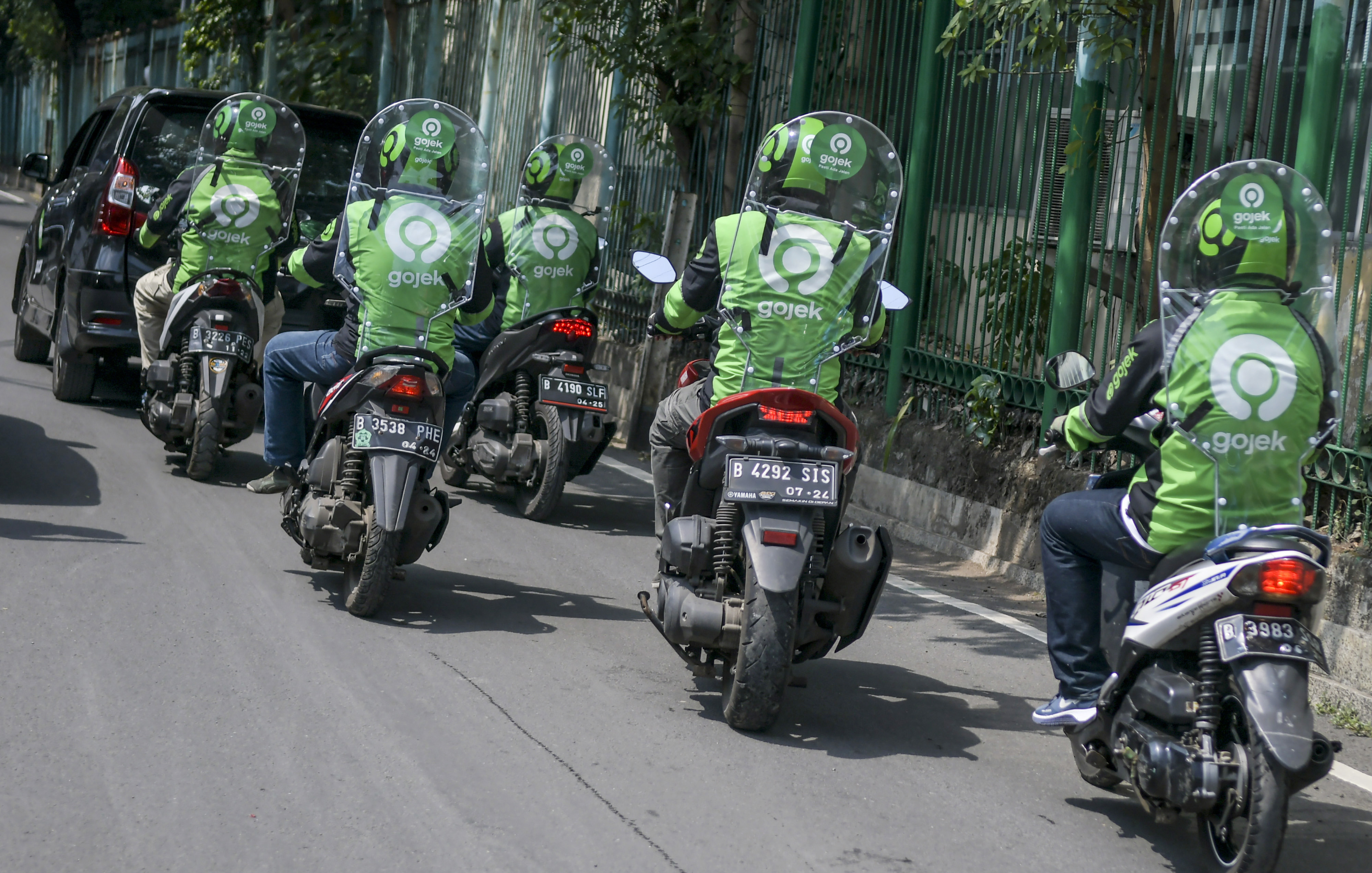 Pengemudi ojek daring mengenakan sekat pelindung saat melintas di kawasan jalan Kendal, Jakarta.