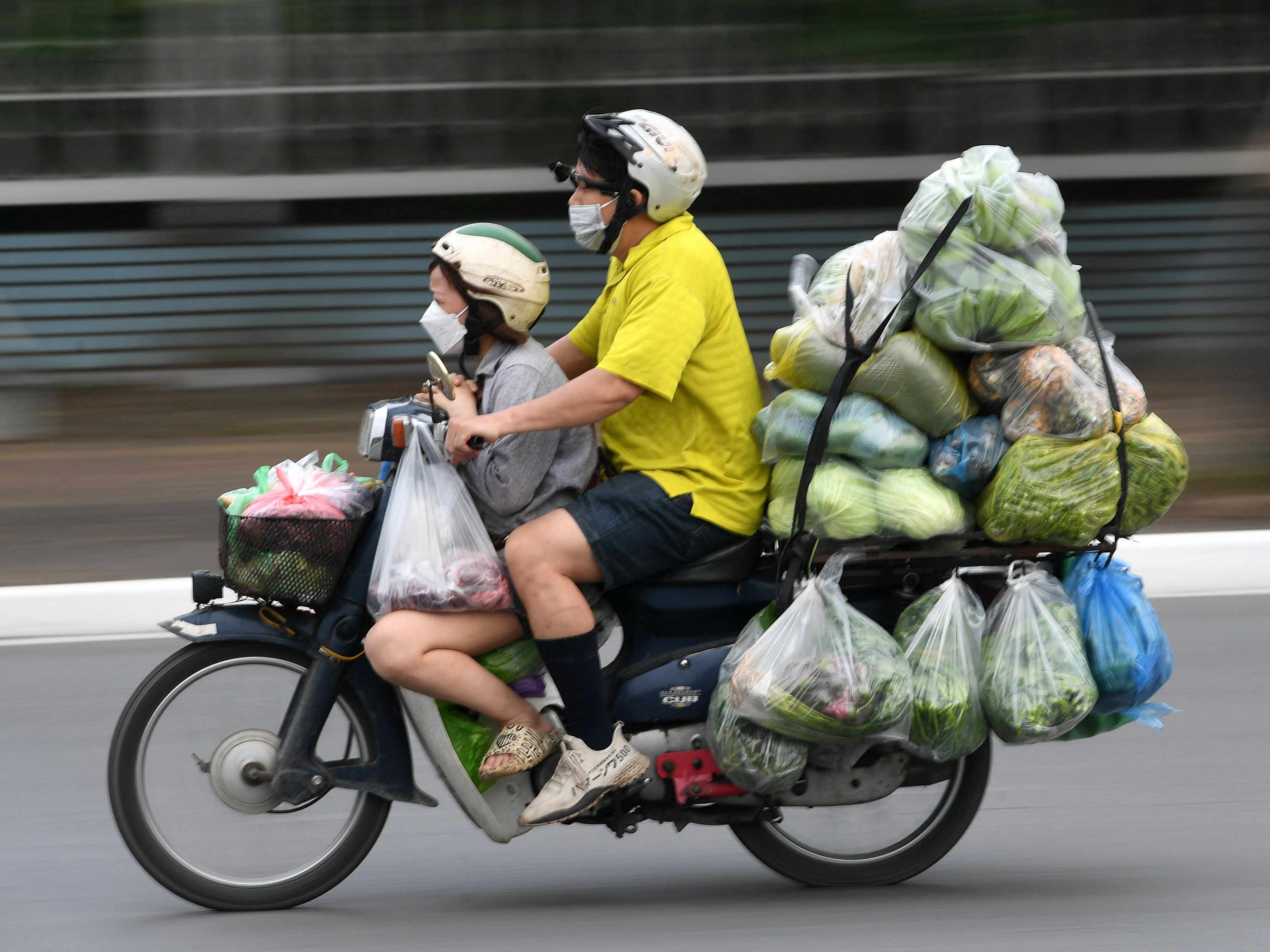 Seorang pria mengendarai sepeda motornya yang penuh dengan sayuran di sepanjang jalan di Hanoi pada 11 Mei 2022. 