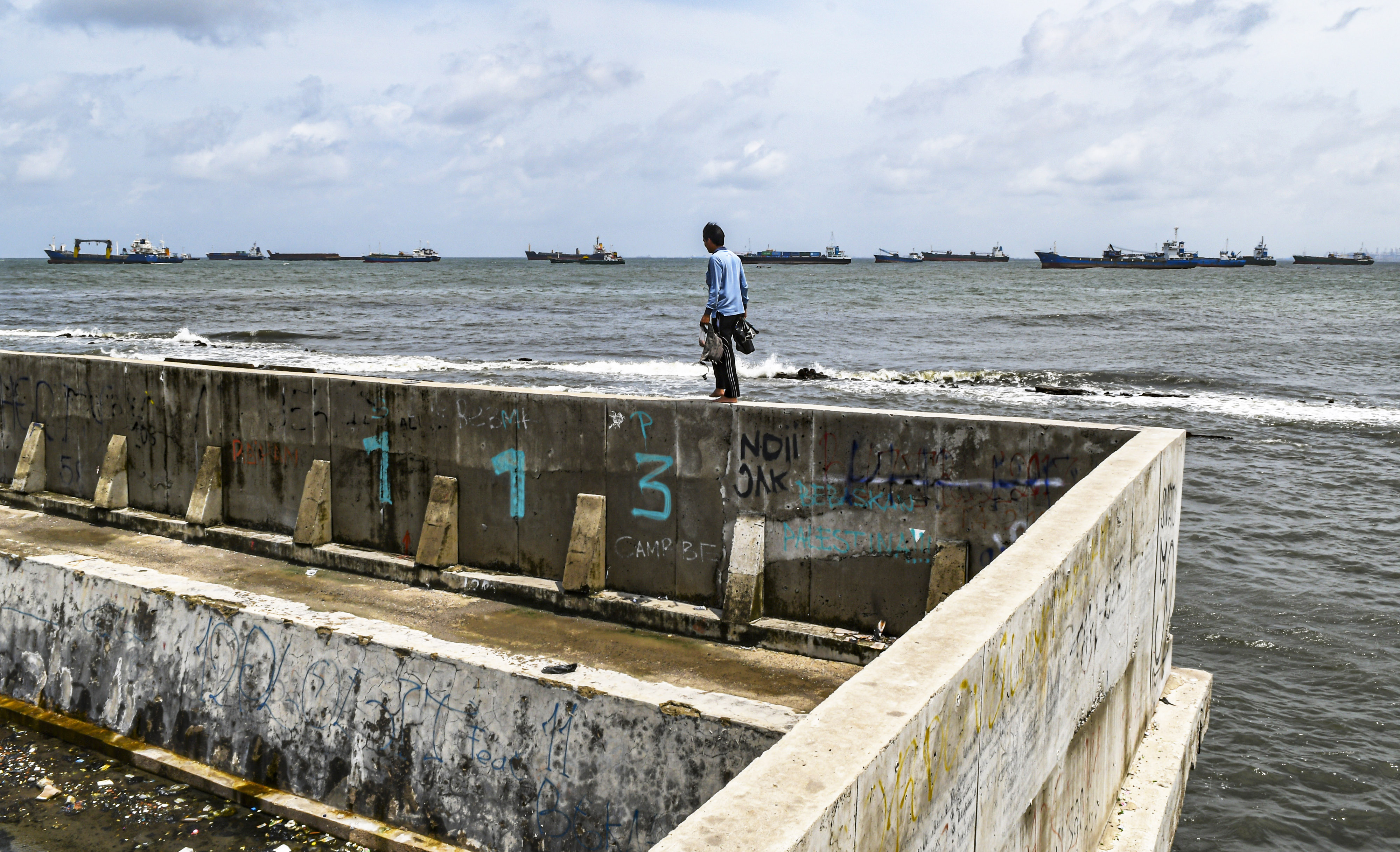 Warga berjalan di tanggul pembatas laut di Muara Baru, Jakarta