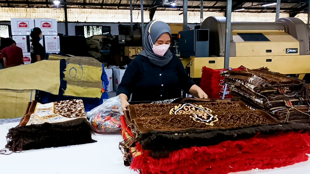 Seorang pekerja tengah menyusun sajadah yang baru selesai dibuat.