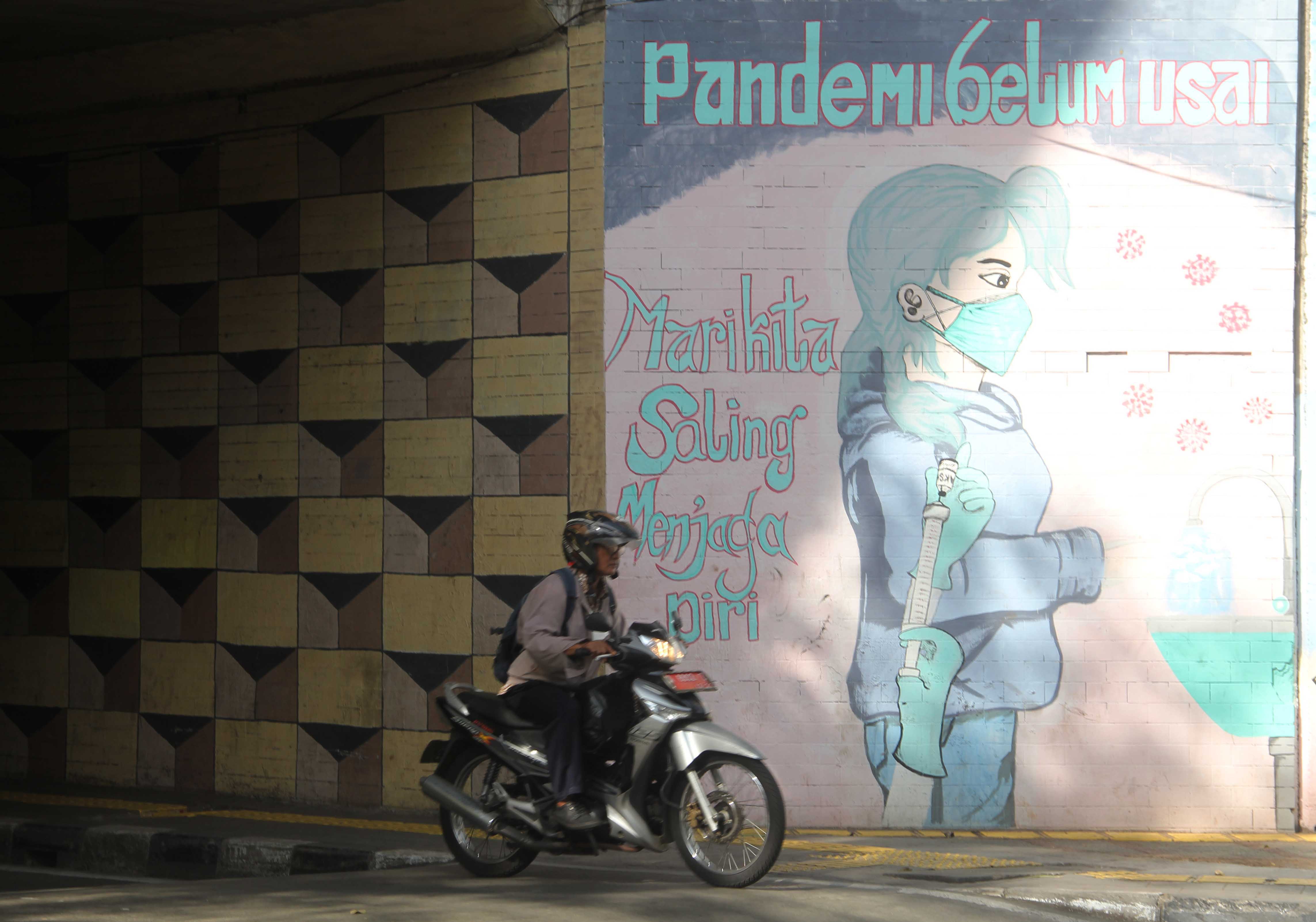 Warga melintasi mural edukasi pencegahan dan perketat protokol kesehatan di Jalan Cikoko Timur, Jakarta.