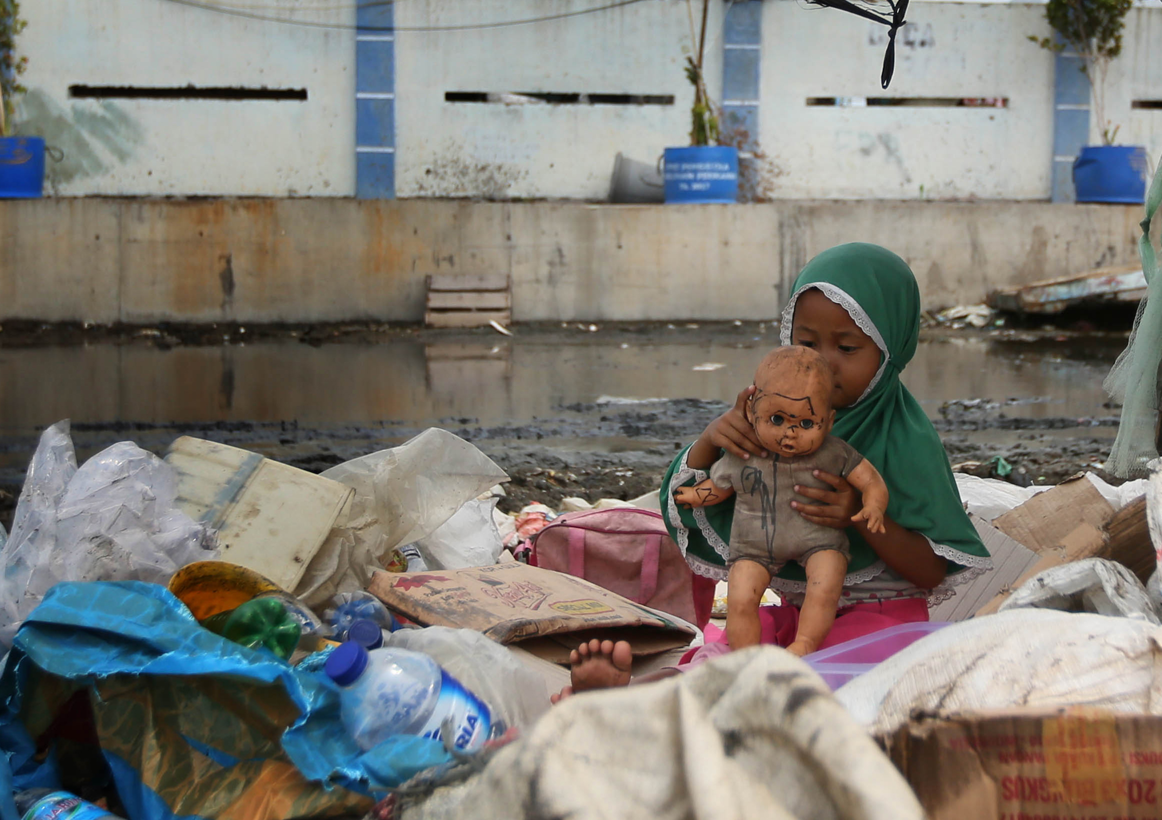 Seorang anak menunggu orangtuanya yang bekerja sebagai pemulung di antara tumpukan barang bekas dan gerobak di kawasan Muara Angke, Jakarta 