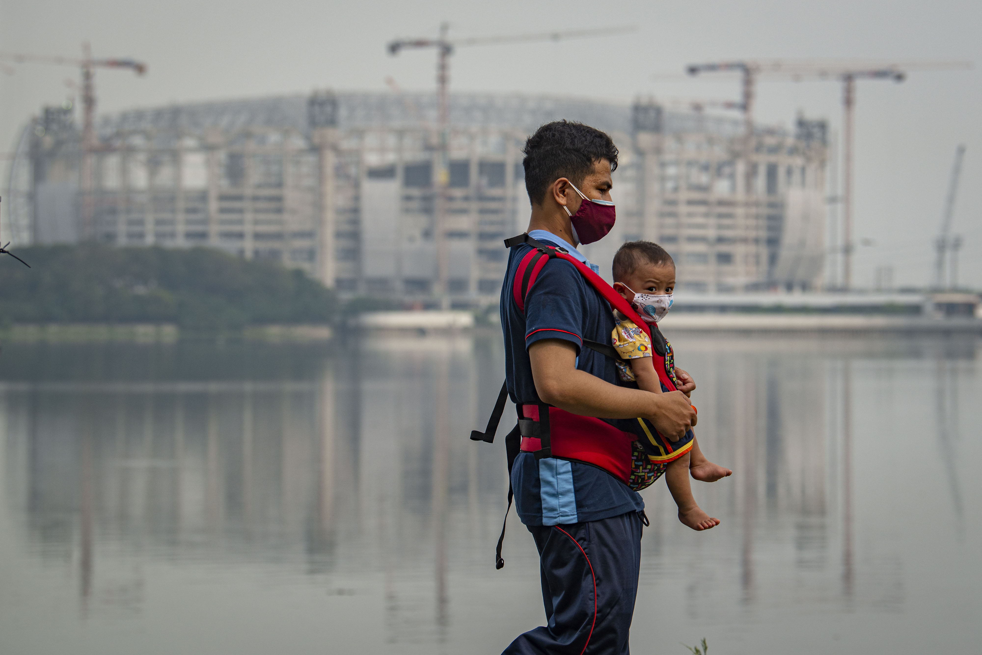 Warga menggendong anaknya saat berjemur di tepi Danau Cincin, Tanjung Priok, Jakarta, Sabtu (24/7/2021).