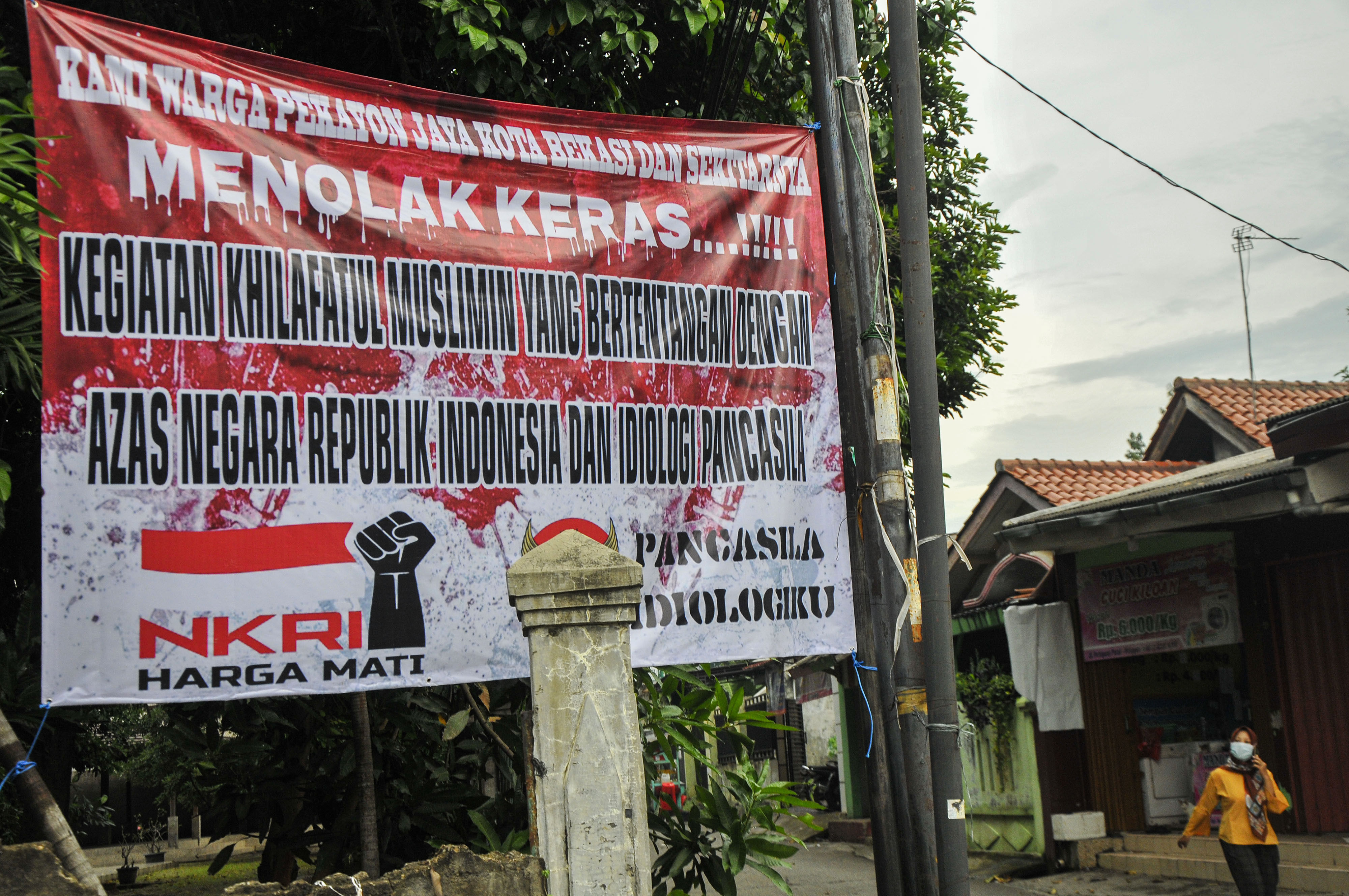 Warga melintas di samping spanduk penolakan kegiatan pendidikan Khilafatul Muslimin di Pekayon, Bekasi, Jawa Barat.