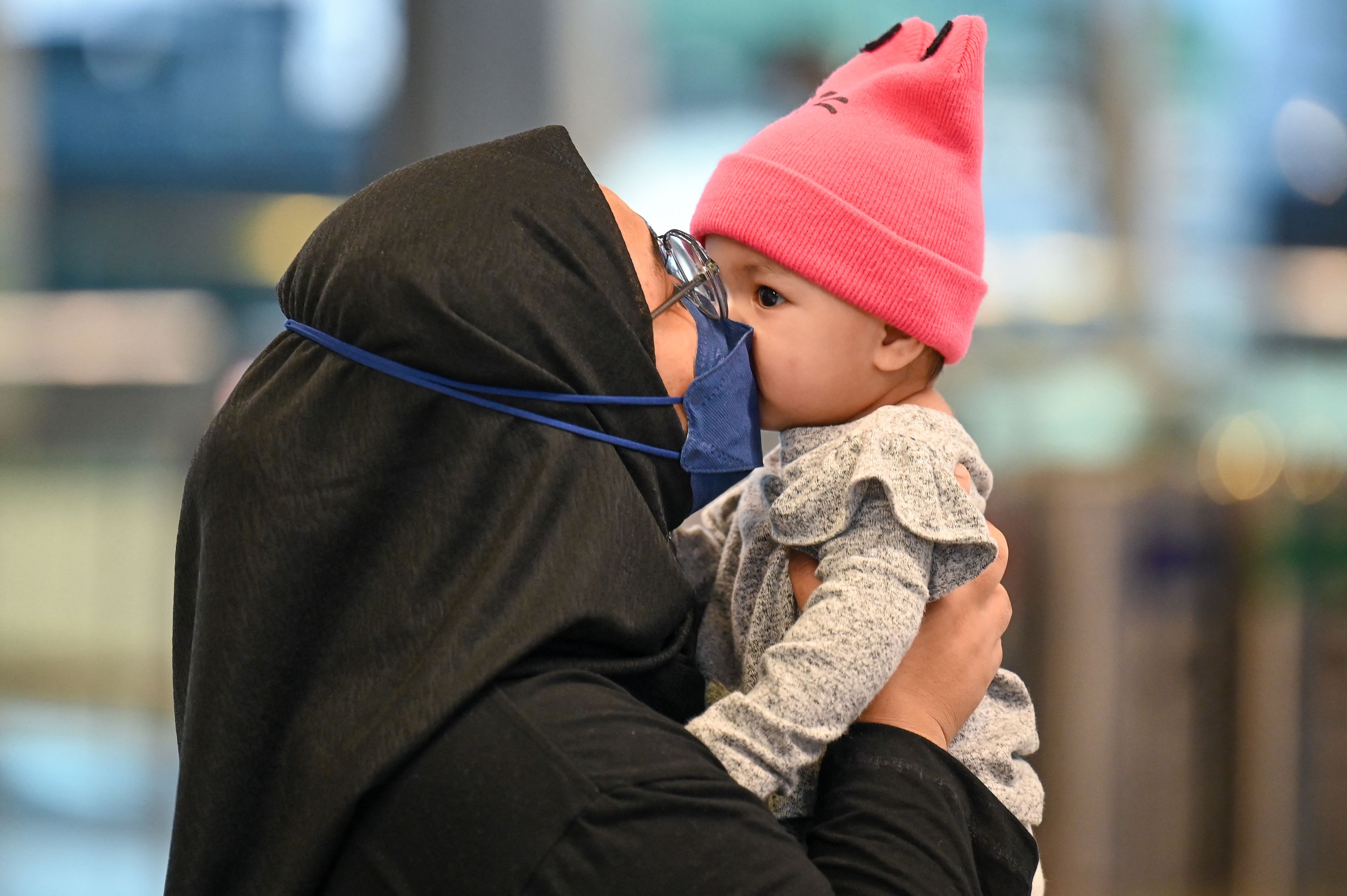 Seorang warga yang memakan masker mencium balita di Bandara Internasional Kuala Lumpur, Malaysia.