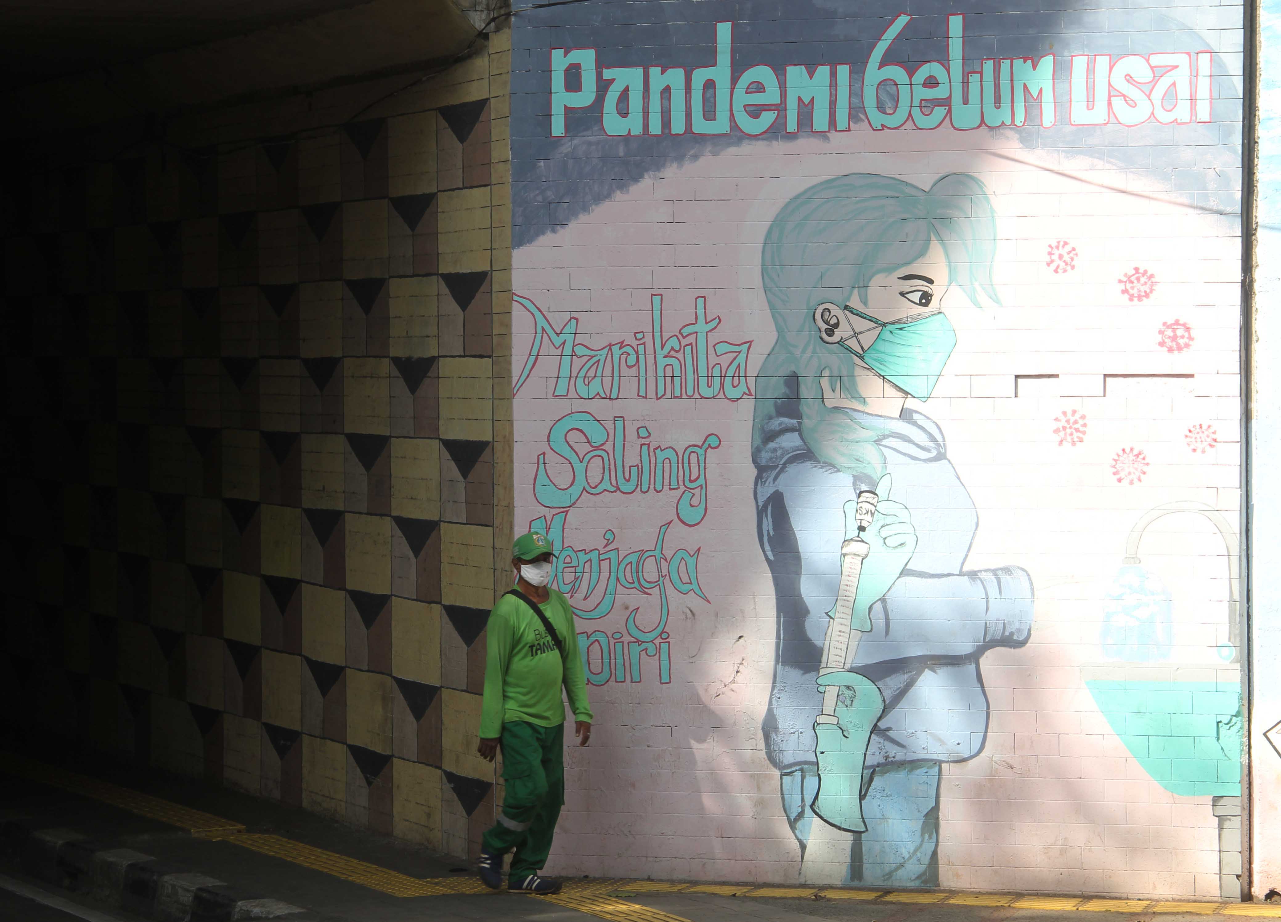 Warga melintasi mural edukasi pencegahan dan perketat protokol kesehatan di Jalan Cikoko Timur, Jakarta.