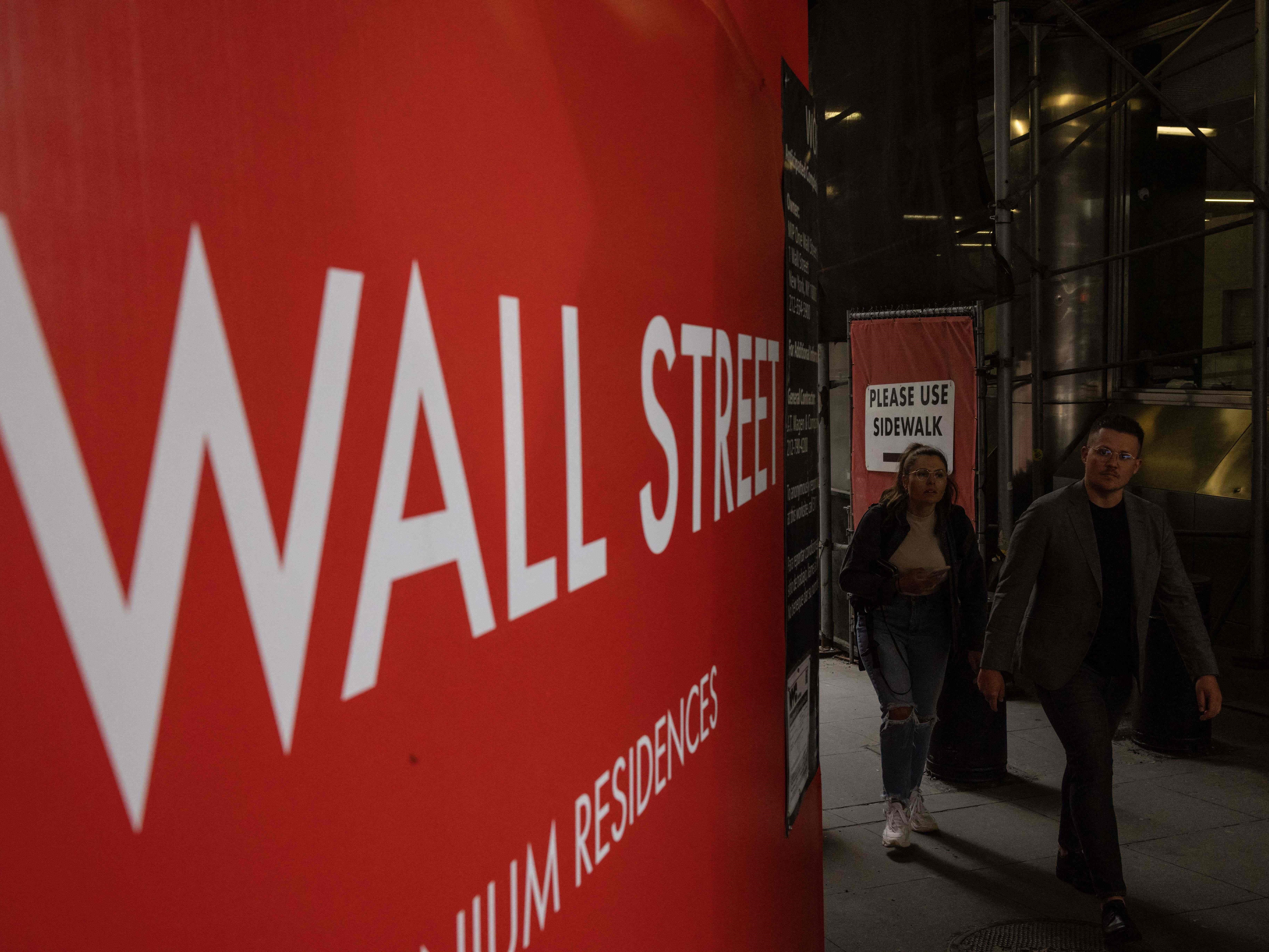 Orang-orang berjalan di sepanjang papan nama Wall Street di New York pada 16 Juni 2022.