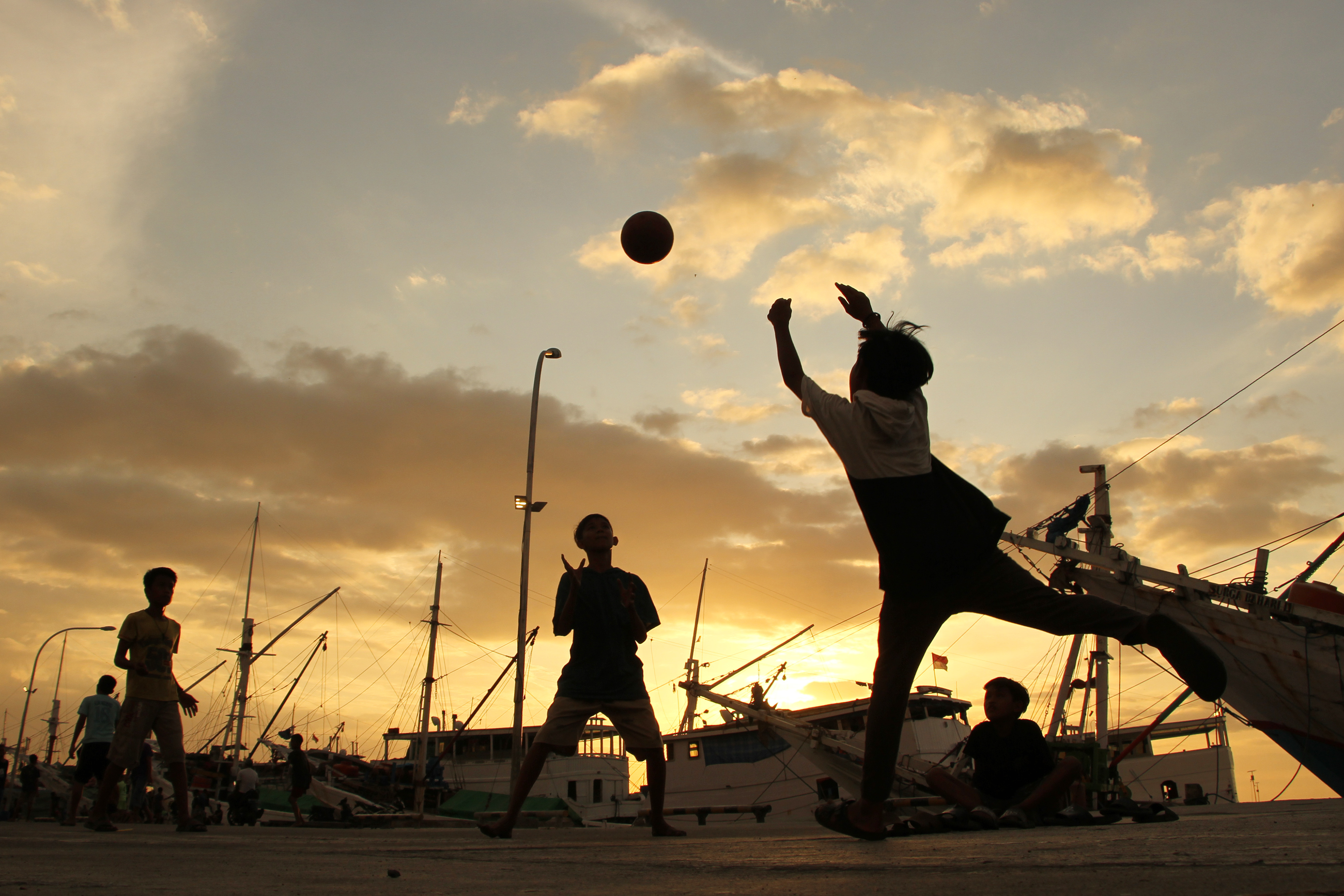 Ilustrasi sejumlah anak bermain sepak bola di dermaga pelabuhan.