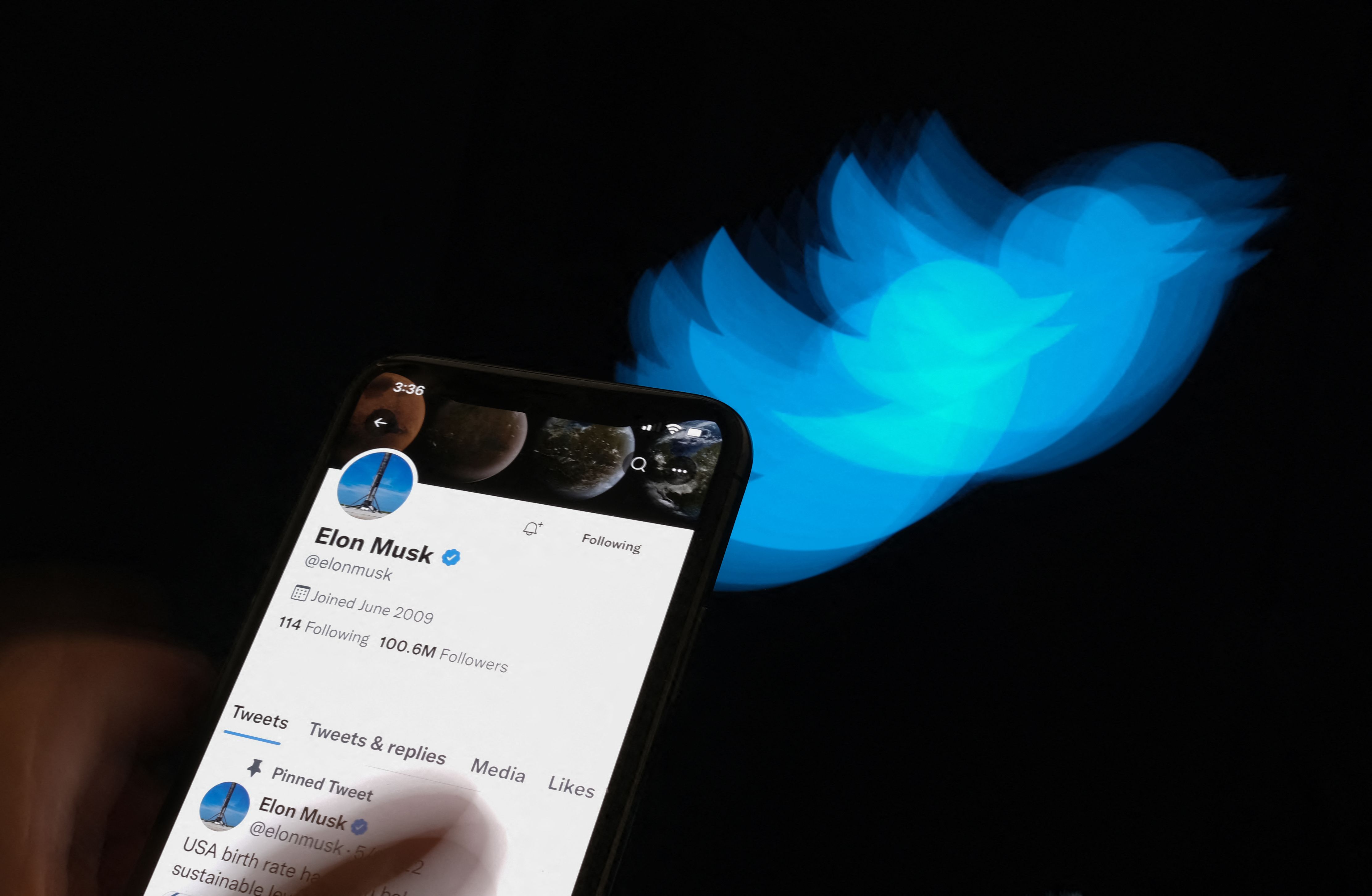 Seseorang memegang ponsel yang menampilkan akun Twitter Elon Musk dengan latar belakang logo Twitter.