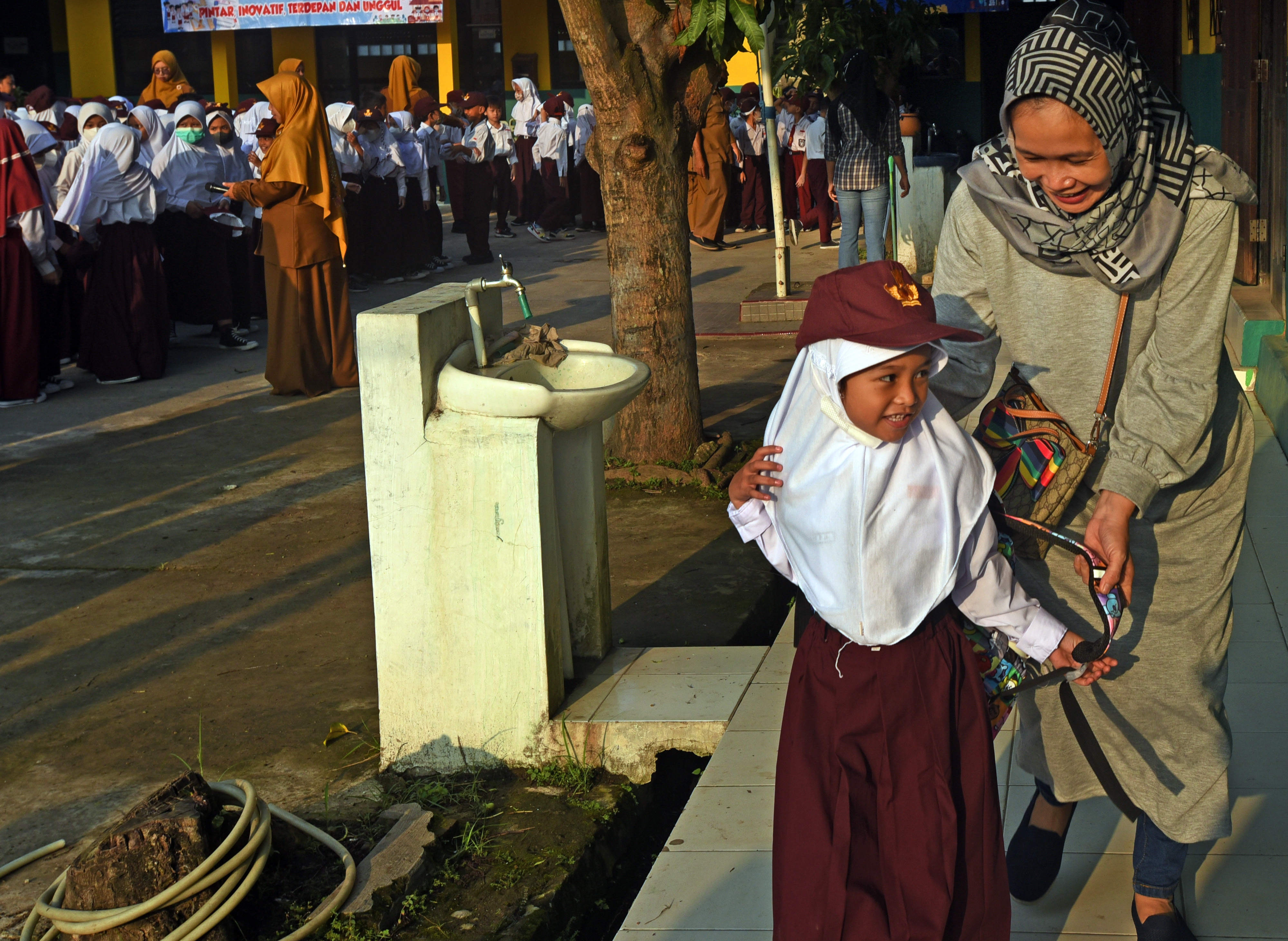 Seorang ibu mengantar puterinya pada hari pertama pembelajaran tatap muka di sekolah.