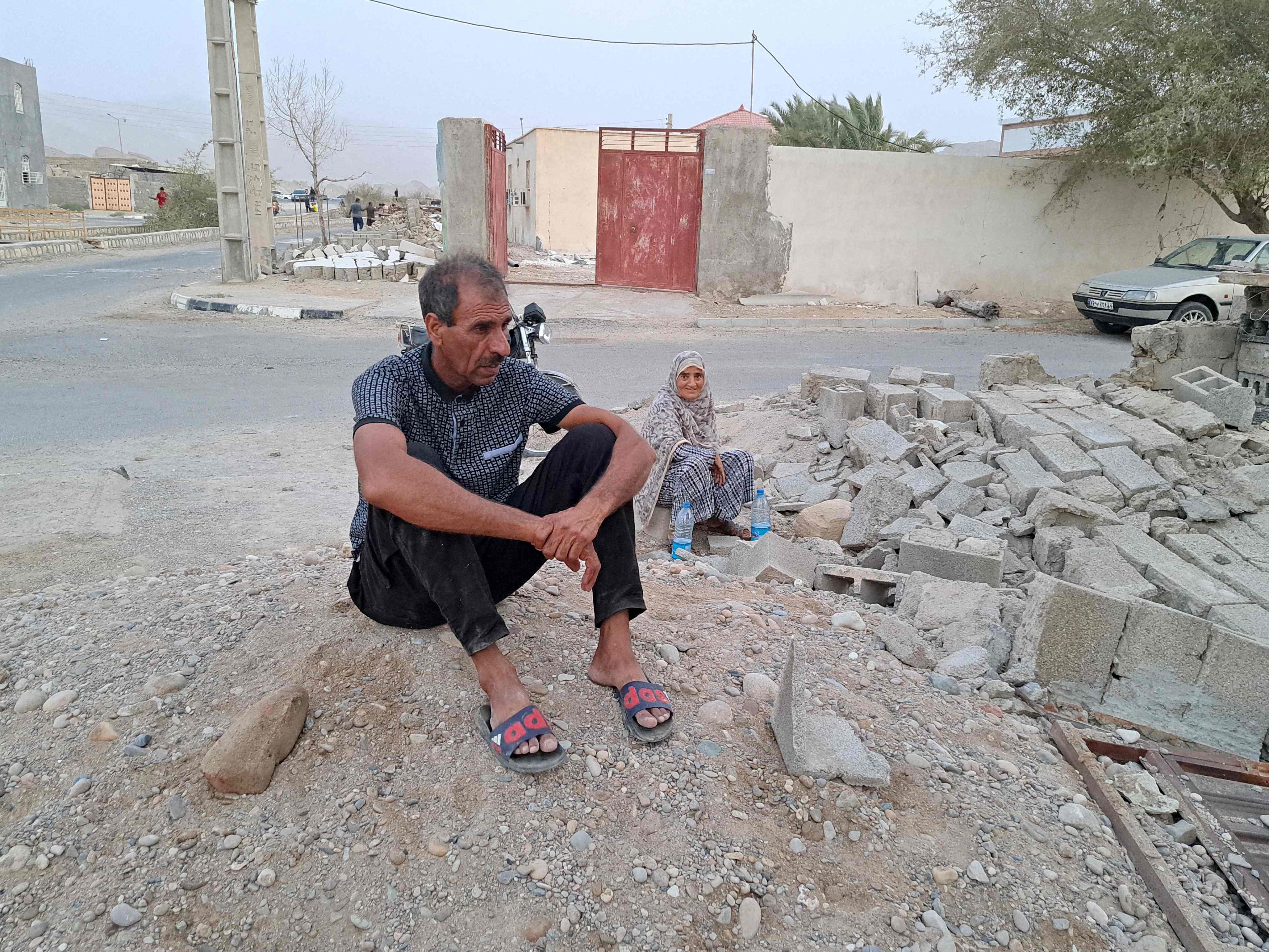 Orang-orang duduk di dekat puing-puing di tengah kehancuran setelah gempa berkekuatan 6,0 di desa desa Sayeh Khosh di provinsi Hormozgan.