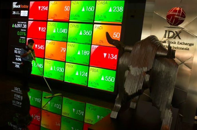 Petugas kebersihan melintasi layar pergerakan saham di gedung BEI, Jakarta.