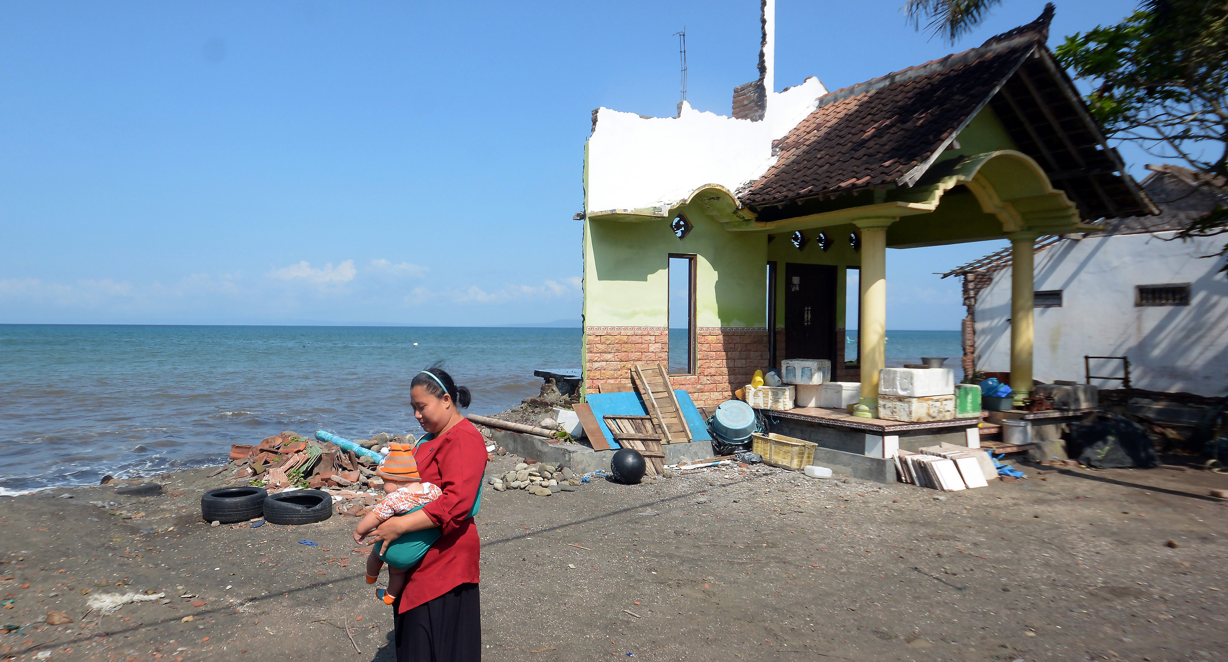 Warga melintas di dekat rumah yang rusak akibat gelombang tinggi di Pantai Pebuahan, Desa Banyubiru, Jembrana, Bali, Rabu (29/6/2022)