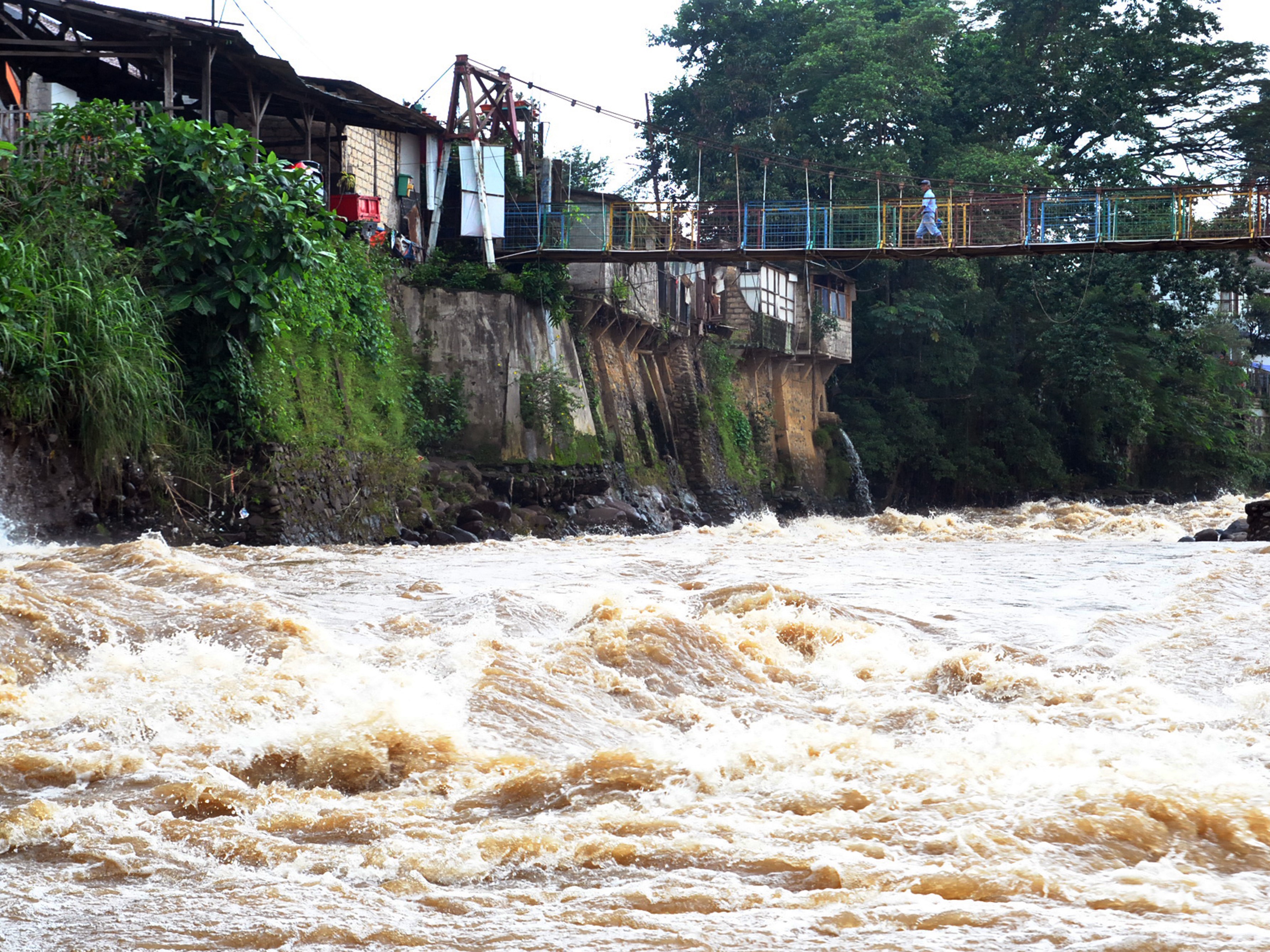  Warga berjalan di atas jembatan sungai Ciliwung yang arus airnya deras, di Kelurahan Sempur, Kota Bogor, Jawa Barat.