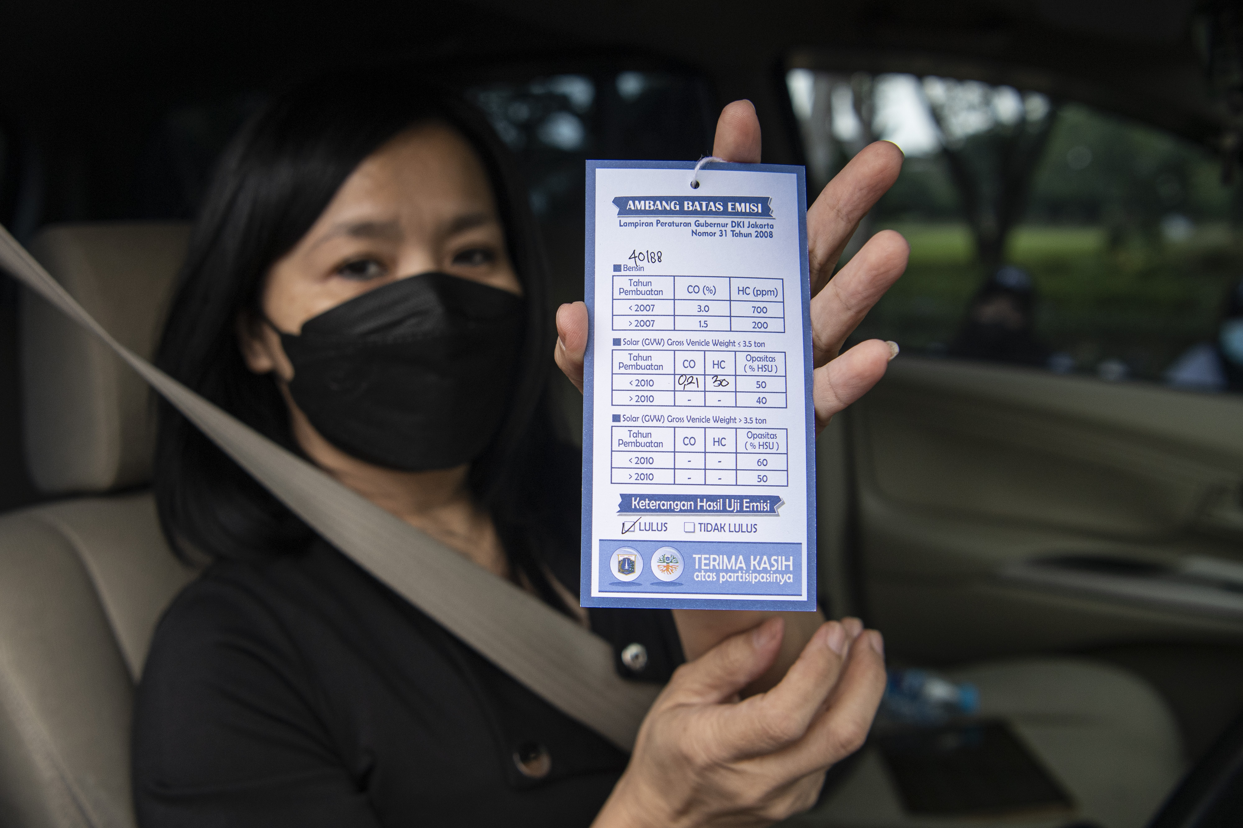 Pengendara mobil menunjukkan kartu hasil uji emisi kendaraannya di Jalan Benyamin Sueb, Pademangan, Jakarta Utara