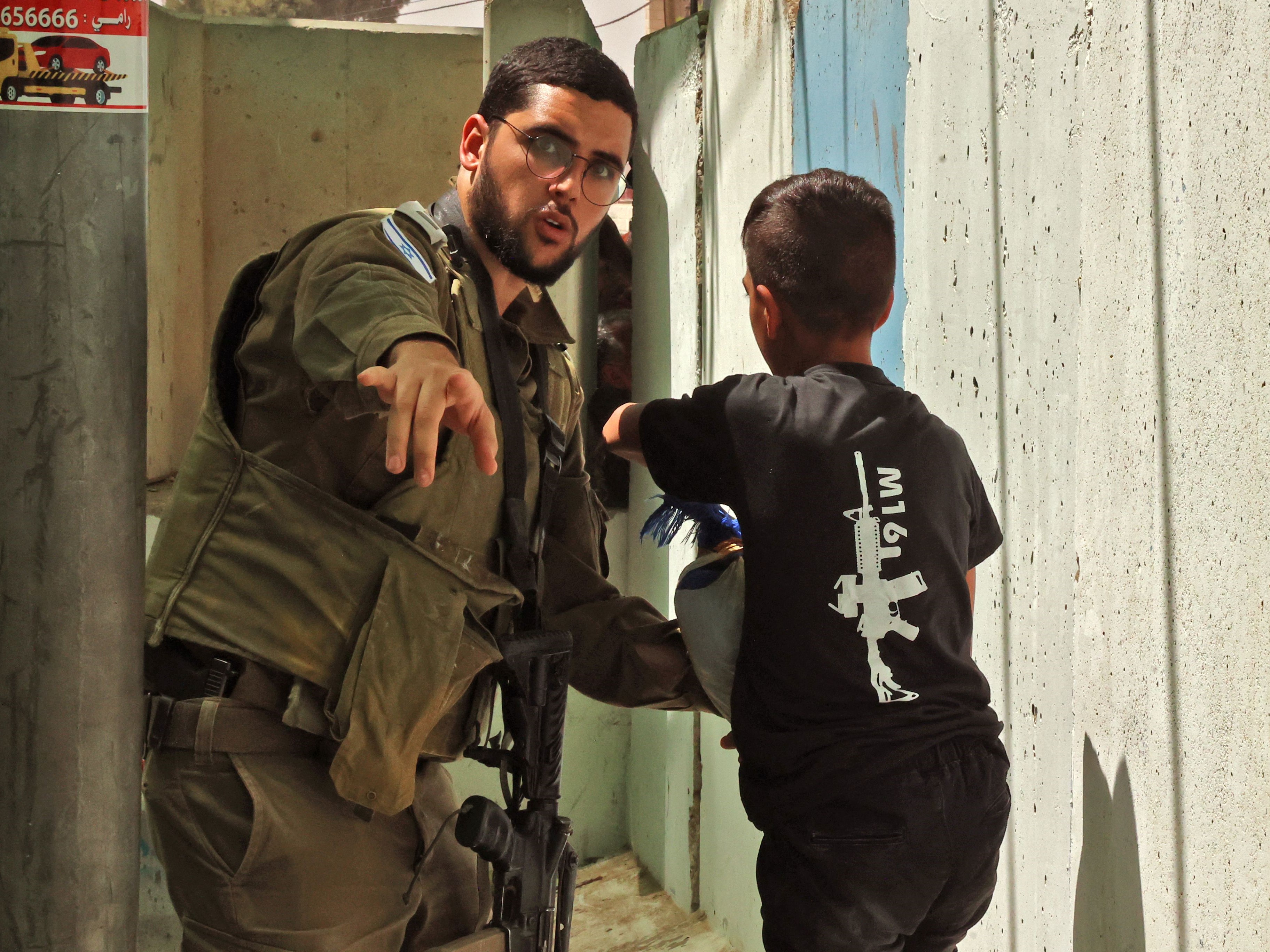 Seorang anak laki-laki Palestina mengenakan kaos yang dicetak dengan senapan M16 di pos pemeriksaan Israel pada 29 April 2022.