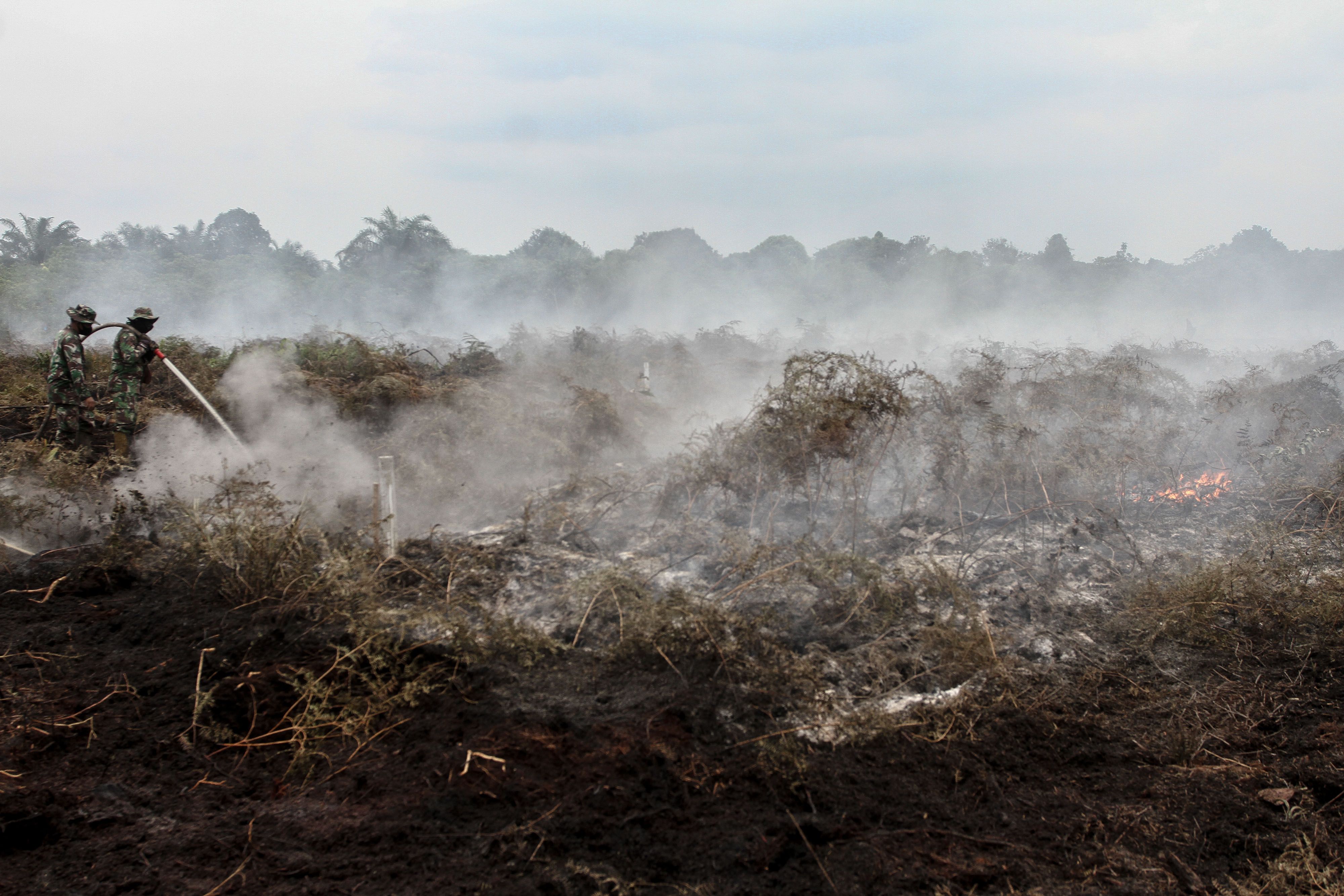Petugas TNI menyemprotkan air untuk memadamkan kebakaran lahan gambut di Kabupaten Kampar, Riau.