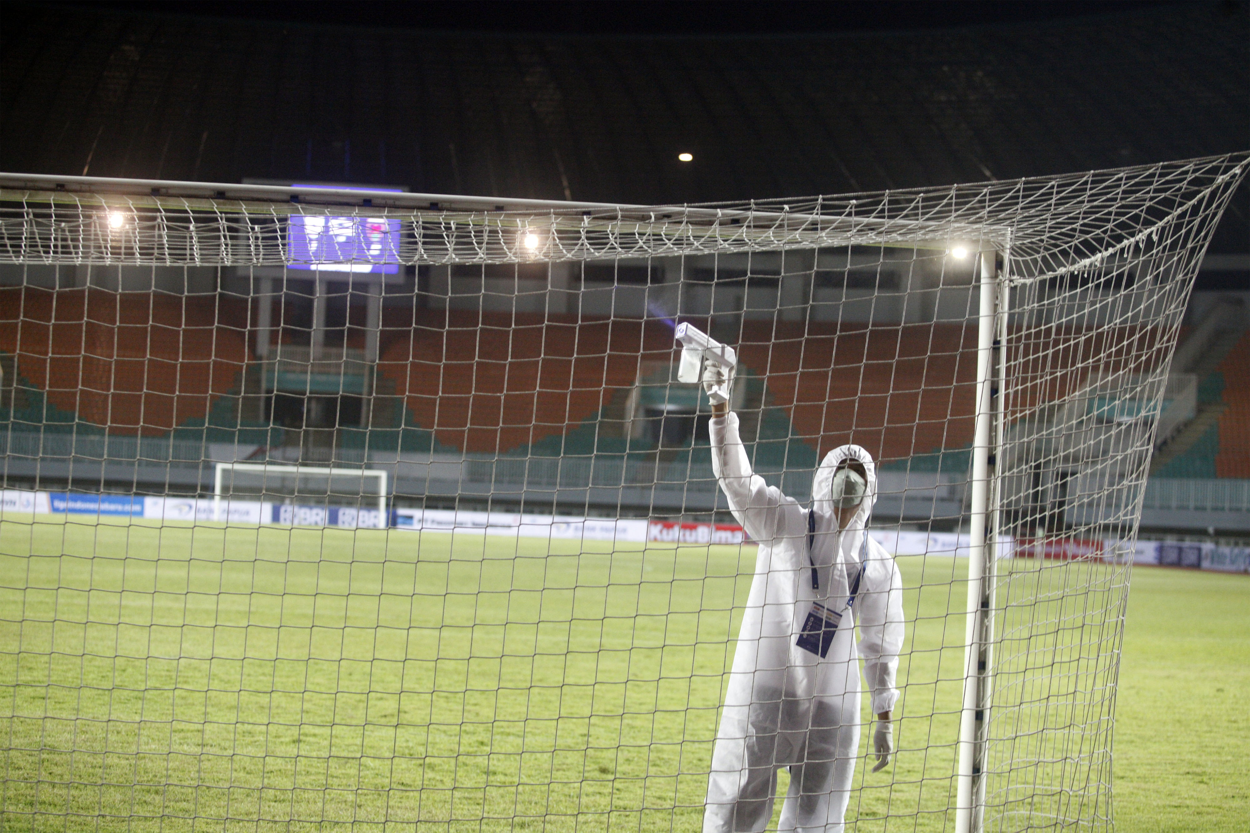 Ilustrasi petugas menyemprotkan cairan disinfektan di lapangan bola.