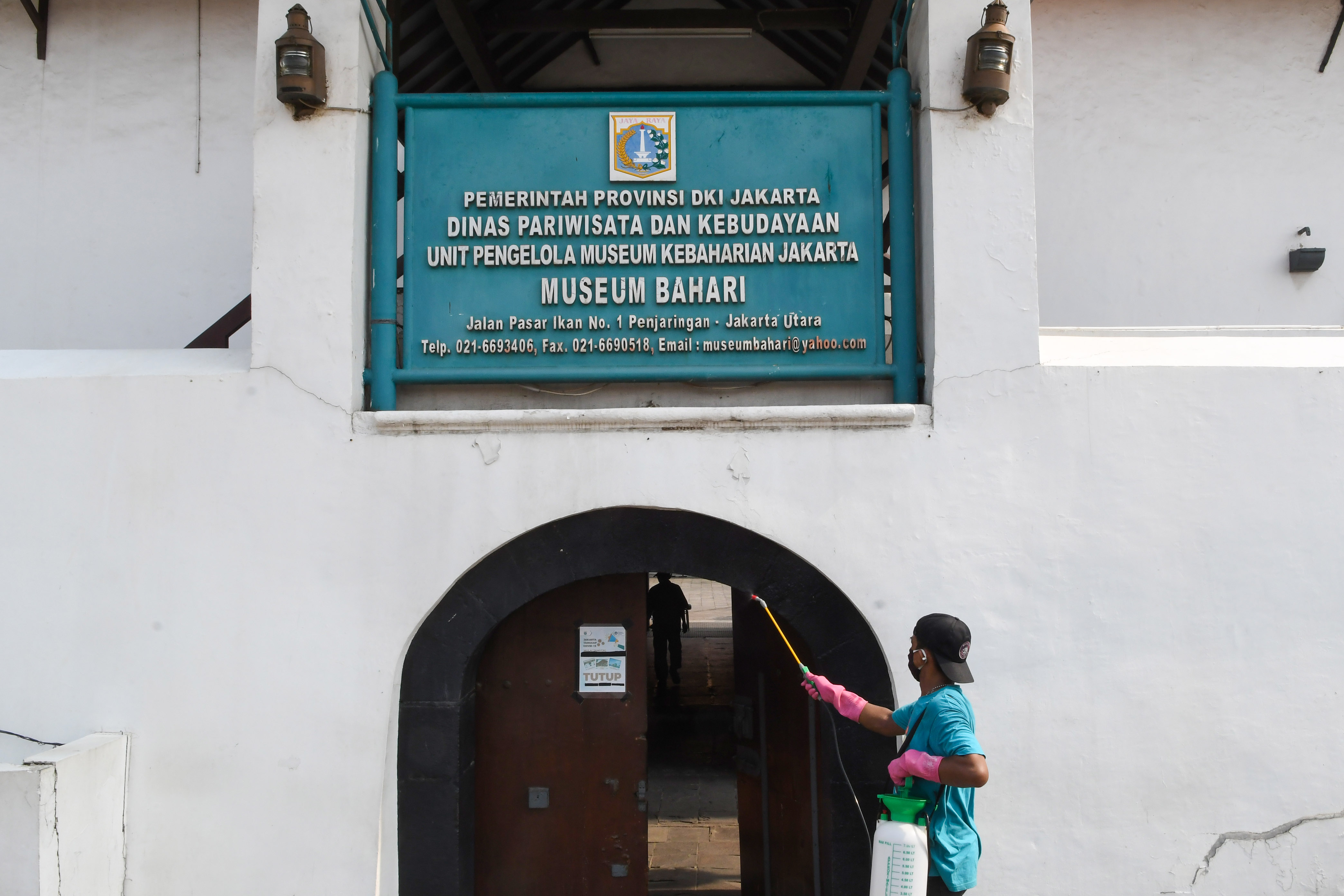  Seorang pekerja menyemprotkan cairan disinfektan pada pintu masuk Museum Bahari, Jakarta, beberapa waktu lalu.