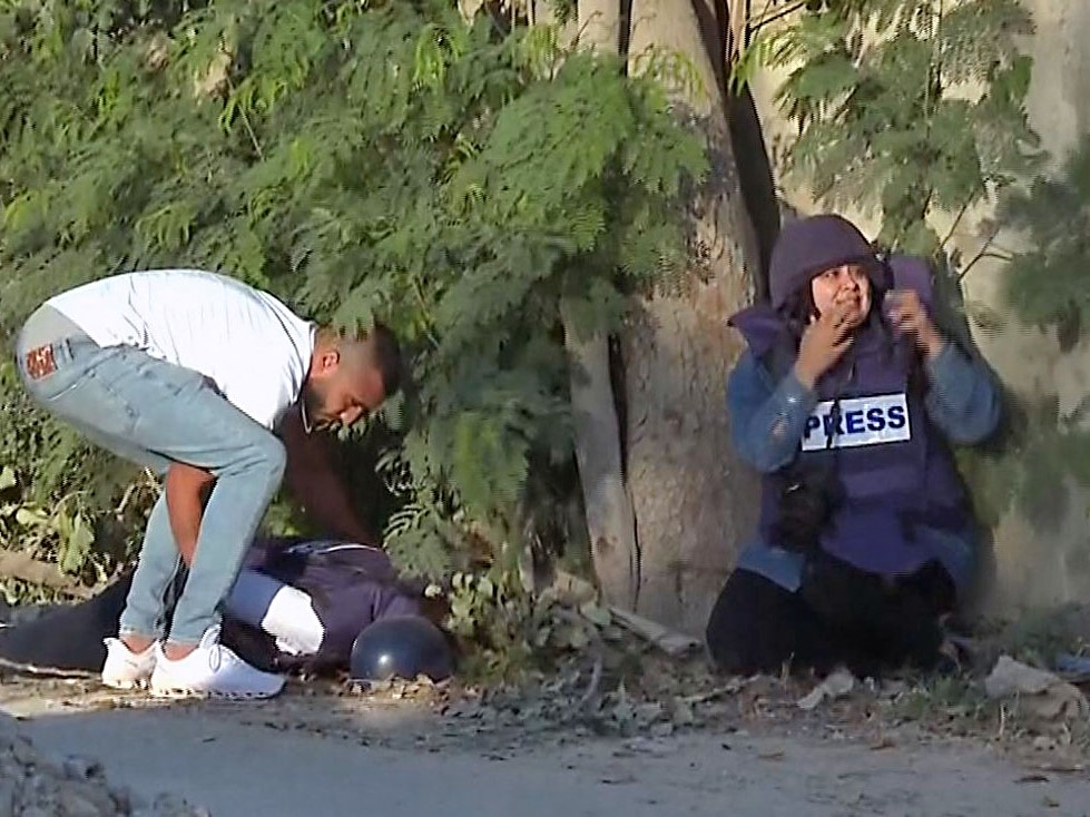 Seorang reporter (kanan) dan seorang pria tak dikenal mencoba mengangkat tubuh jurnalis veteran saluran tersebut Shireen Abu Akleh.
