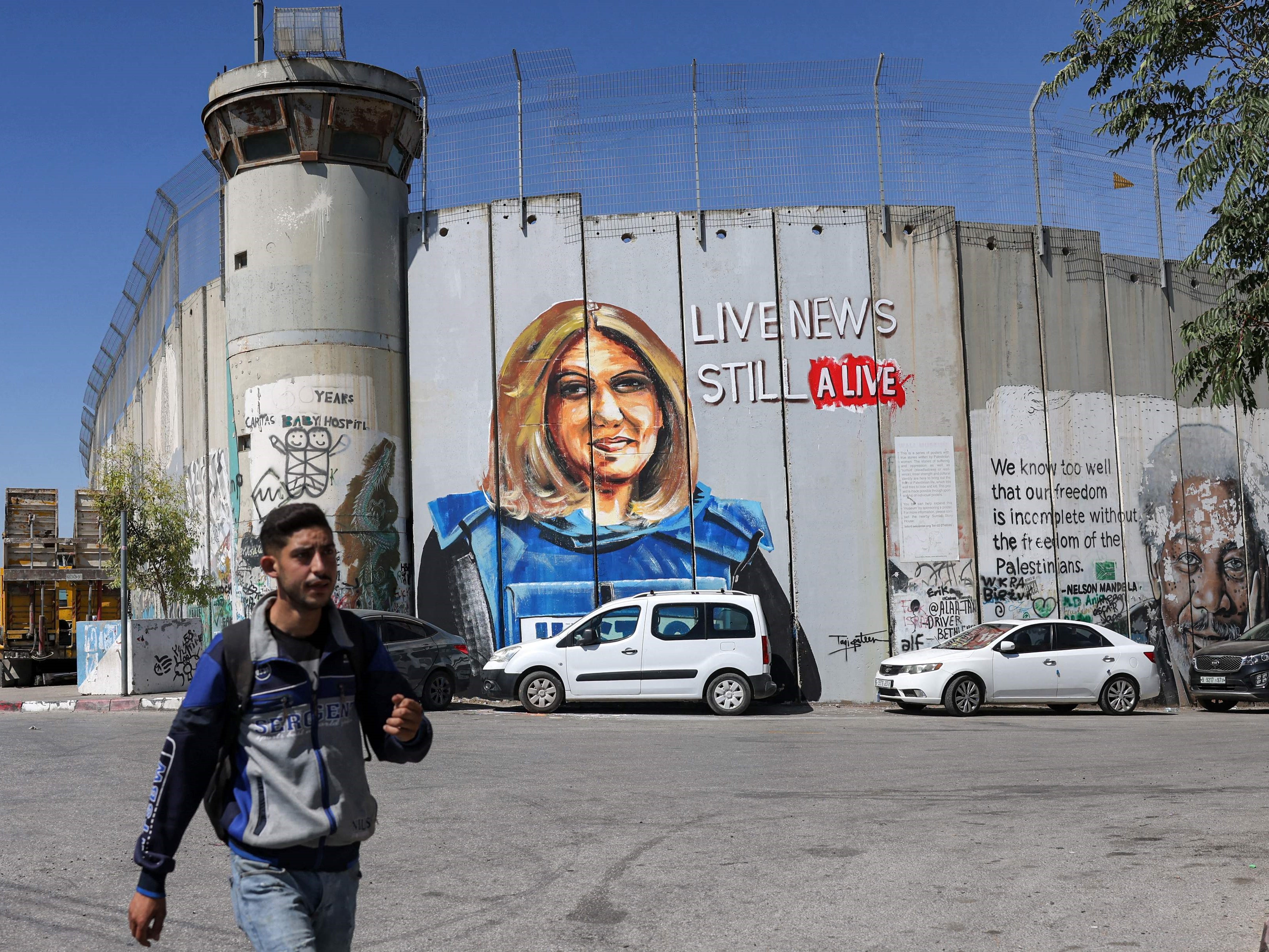 Seorang pemuda berjalan melewati mural yang menggambarkan jurnalis Al Jazeera yang terbunuh Shireen Abu Akleh.