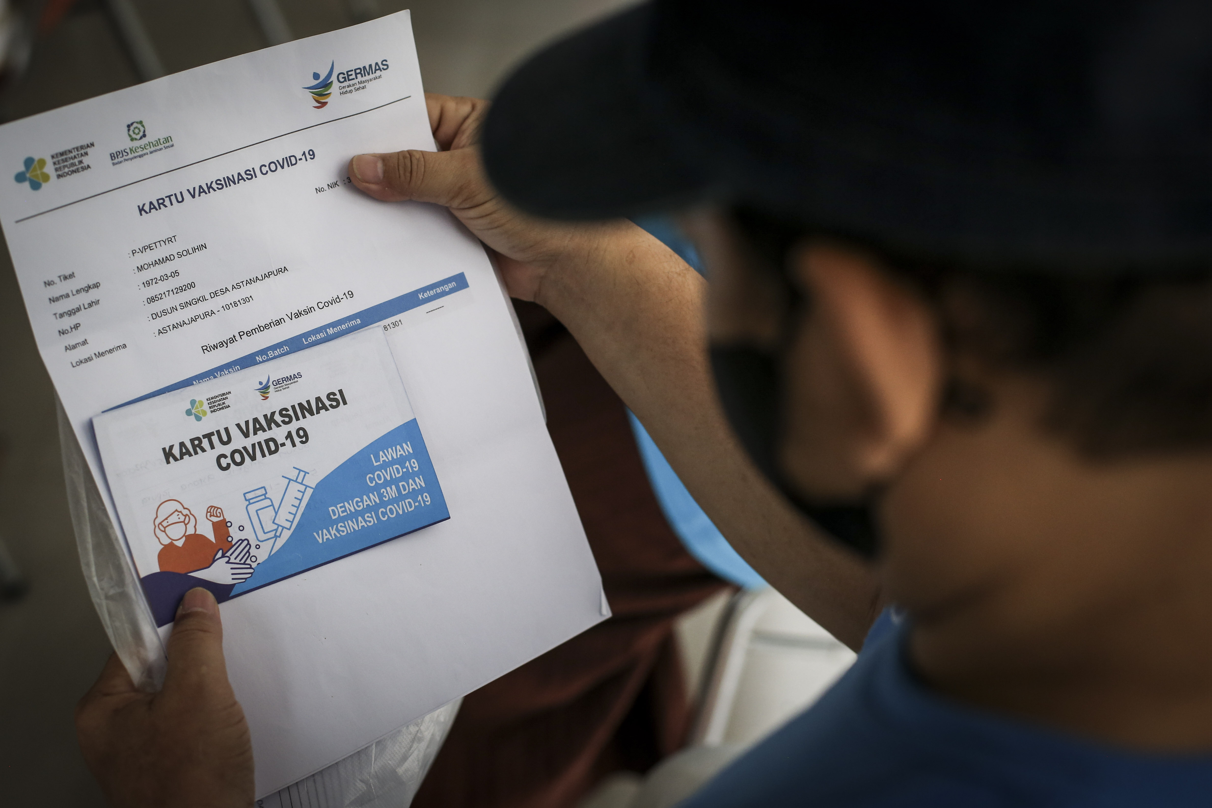 Seorang warga melihat kartu vaksinasi covid-19 dosis ketiga di RPTRA Rusun Benhil, Jakarta, Rabu (6/7).
