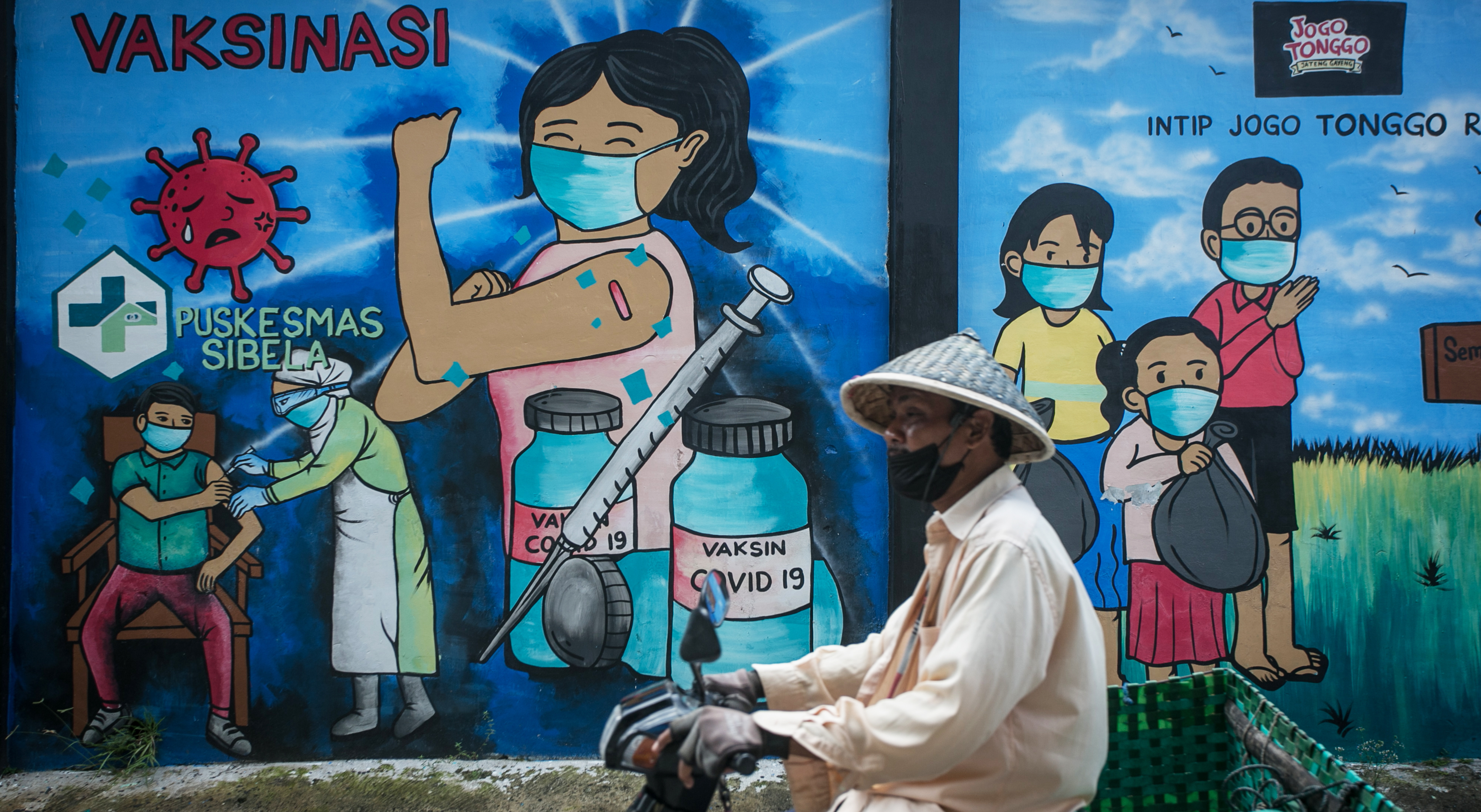 Warga melintas di depan mural bertema ajakan vaksinasi di Mojosongo, Solo, Jawa Tengah