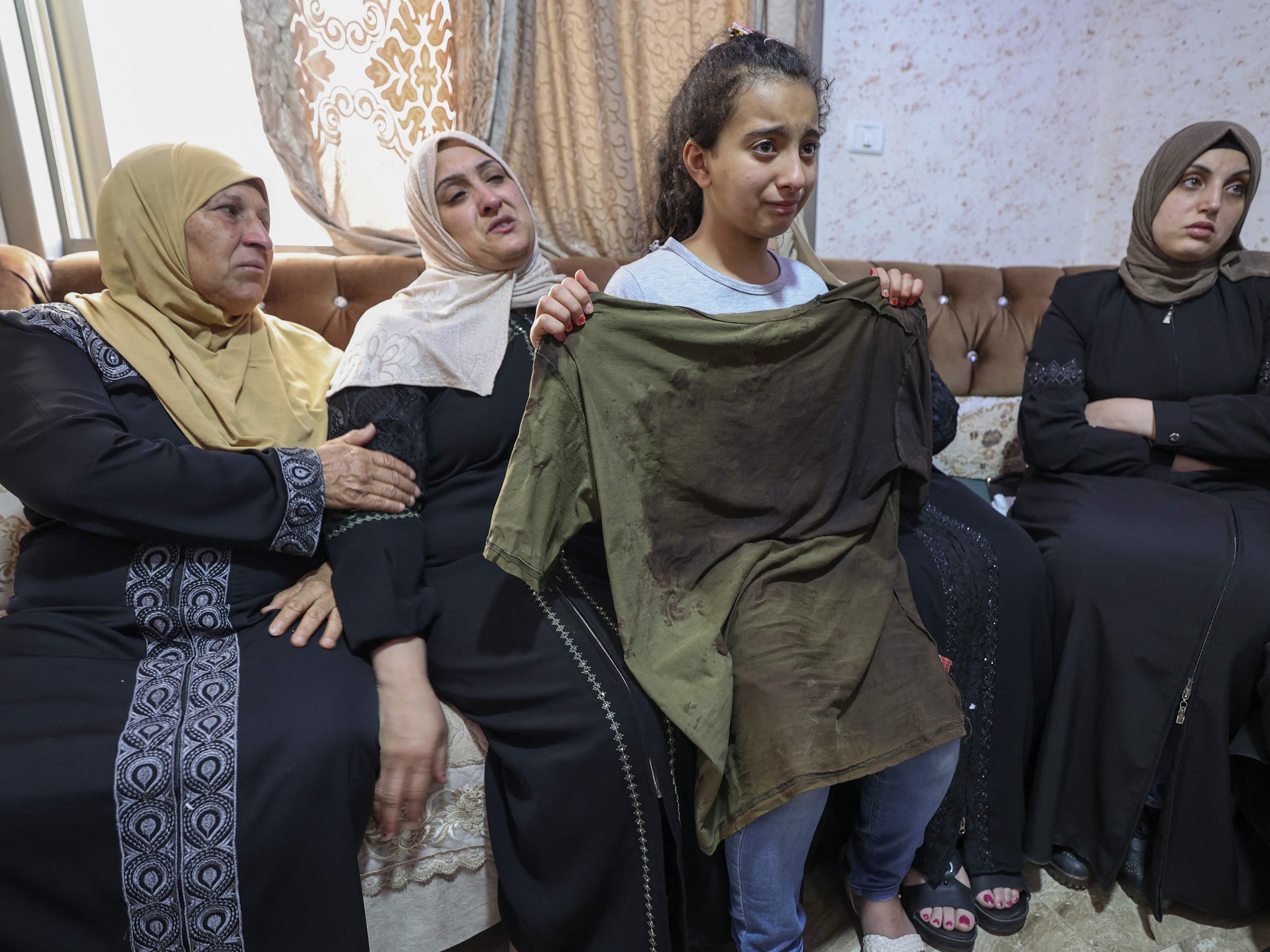 Saudari dari Mohammed al-Shaham, 21, yang tewas dalam serangan rumah Israel, membawa baju saudara laki-lakinya berlumuran darah.