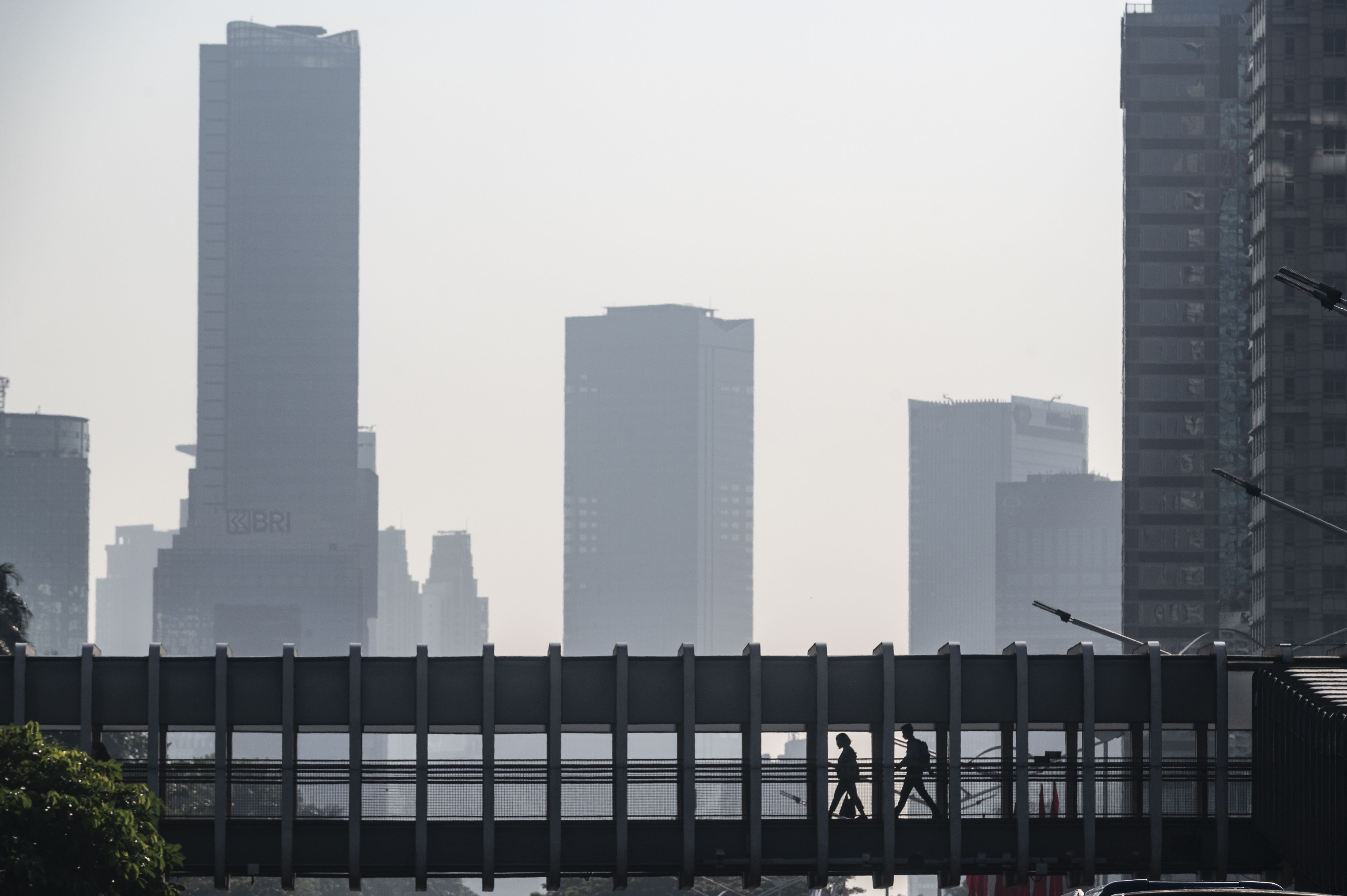 Warga berjalan di jembatan penyeberangan orang dengan latar belakang gedung bertingkat di Jakarta.